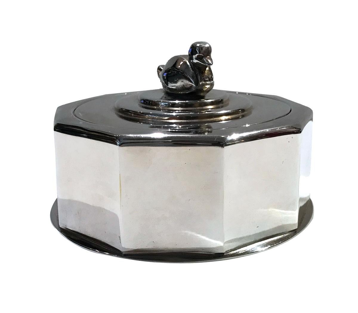 Art Deco silverplated decagonal box on a circular base. The lid is decorated with two round moldings and a stylized duck knob. 
Very beautiful item and rare. Stamped beneath the name of the metal worker 
