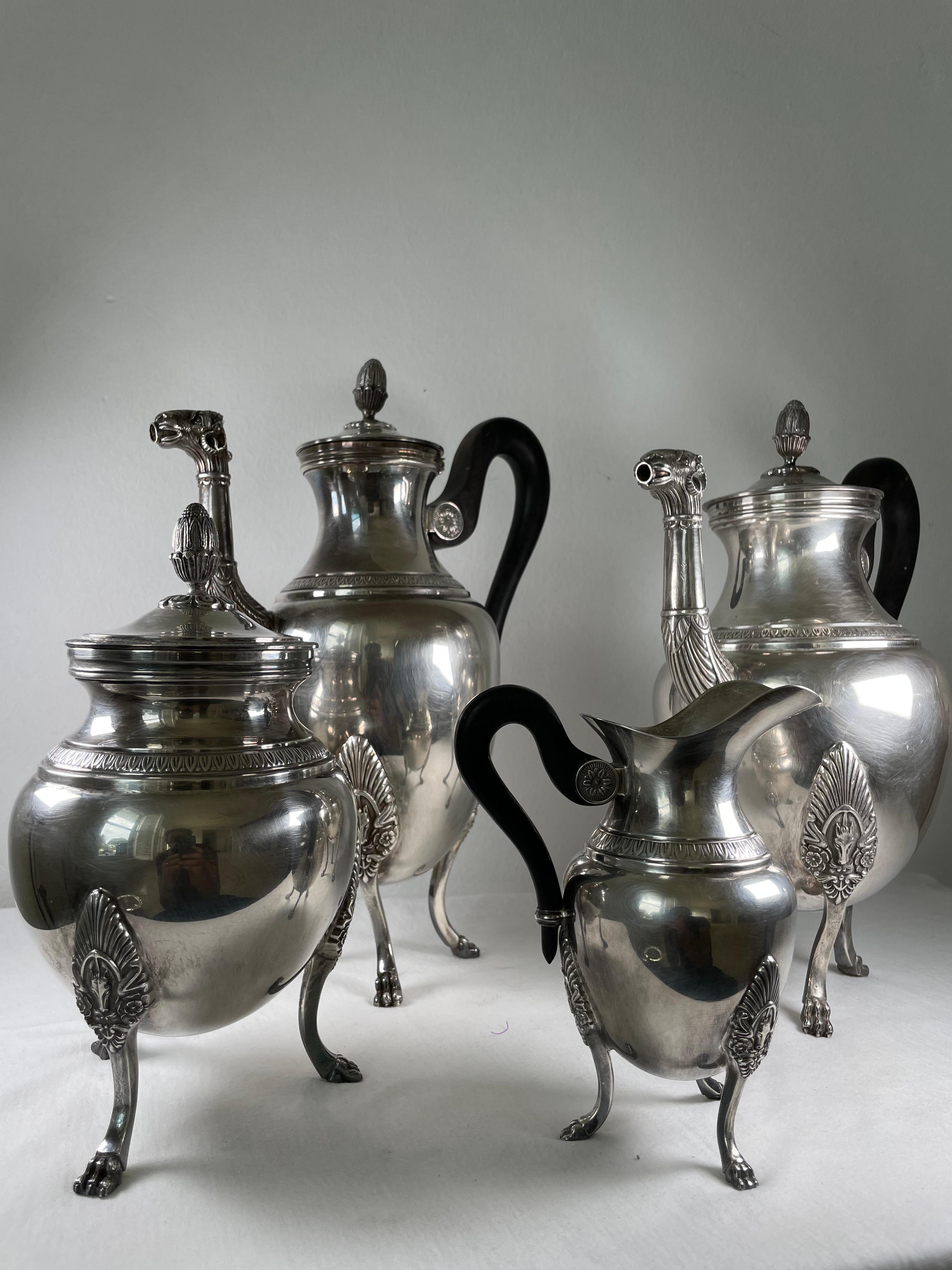 A Christofle 'Malmaison Empire' four-piece coffee and tea set. It features a black-handled teapot and coffee pot, both of which have camel head-shaped spouts, and a lidded sugar bowl and milk pot. All of the pieces Stand on three decorative feet