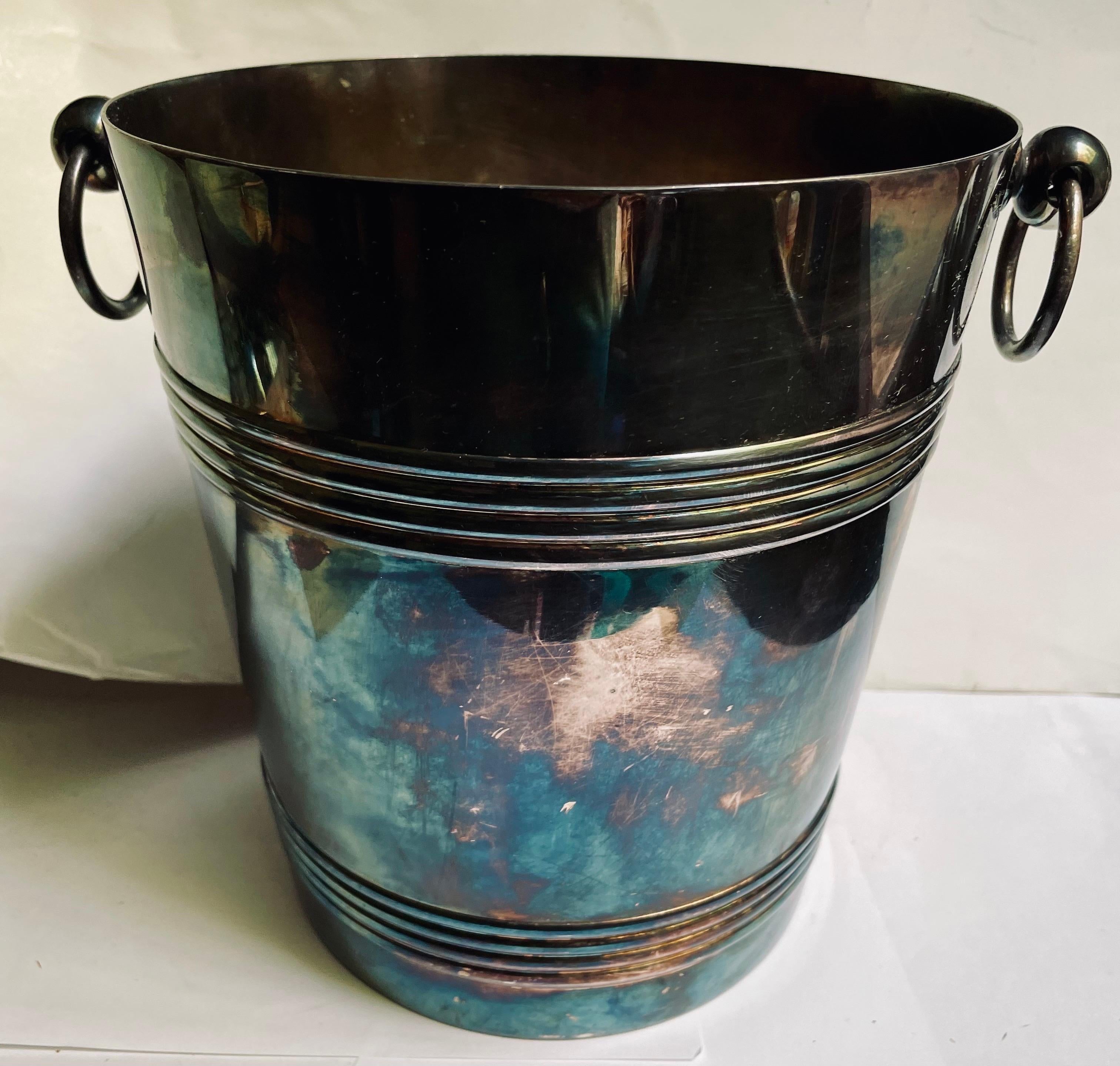 Ein klassischer, schlichter, aber eleganter Eis- oder Sektkübel mit erhabenen Rippen, die den Körper im oberen und unteren Bereich umschließen, und einfachen Griffen mit Tropfenring an beiden Seiten. Das Stück ist von feiner Qualität, wie man es von