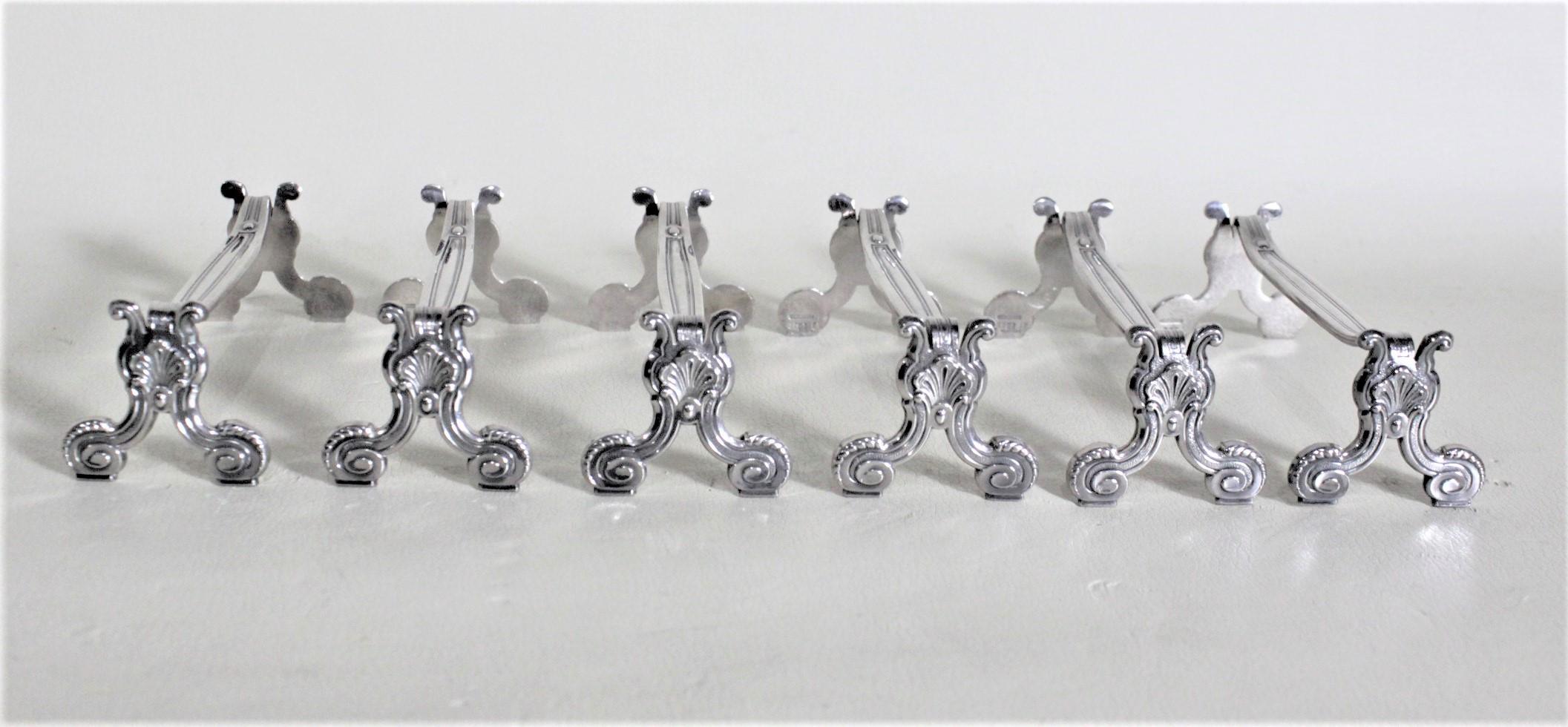 This set of six silver plated knife rests were made by Christofle of France in approximately 1960 in an antique style. The knife rests have nicely decorated serpentine side panels with rounded feet and platform stretchers. Each knife rest is clearly