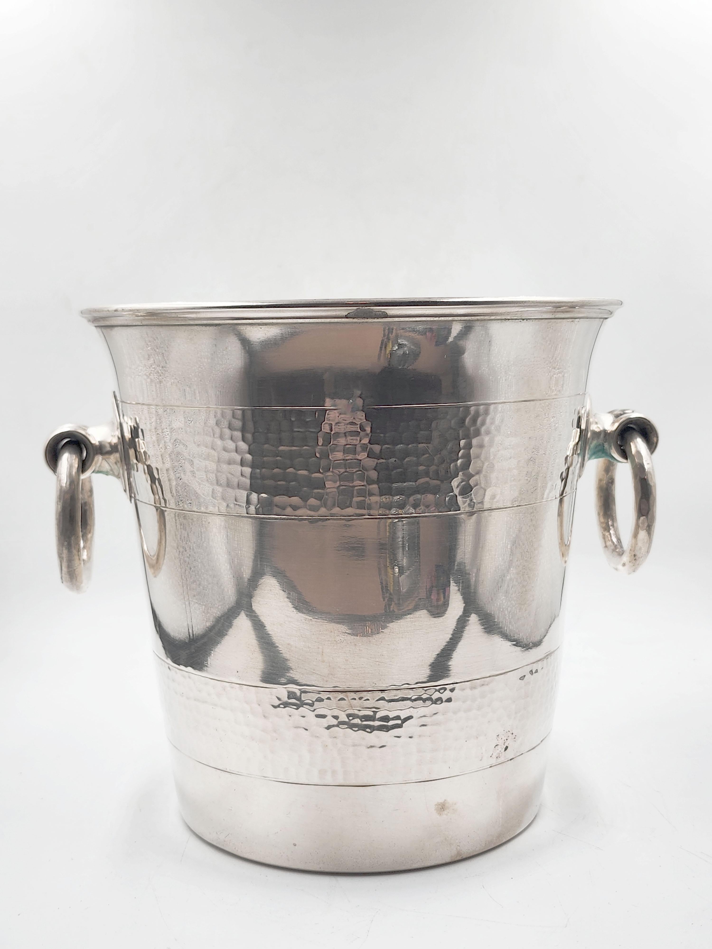 Christofle Versilberter Champagnerkübel aus Metall
Dieser Champagnerkübel von Christofle aus den 1950er Jahren hat ein klassisches und elegantes Design. Er ist aus versilbertem Metall mit einer gehämmerten Struktur gefertigt, die ihm ein
