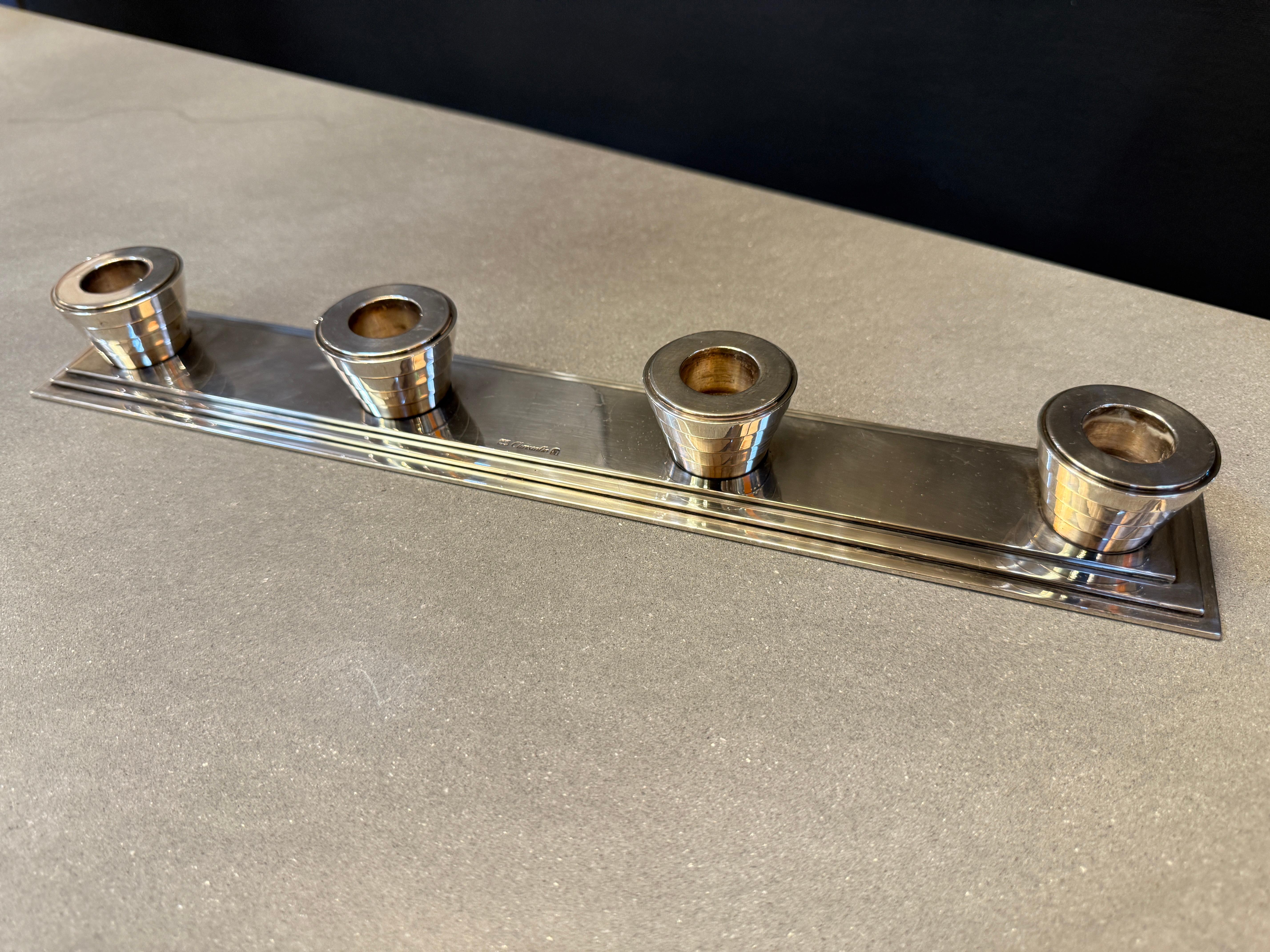 A refined silver-plated candlestick holder by Christofle, featuring four conical candle sockets set on a stepped rectangular base. The sleek, symmetrical design highlights Christofle’s hallmark craftsmanship, combining elegance with a modernist Art