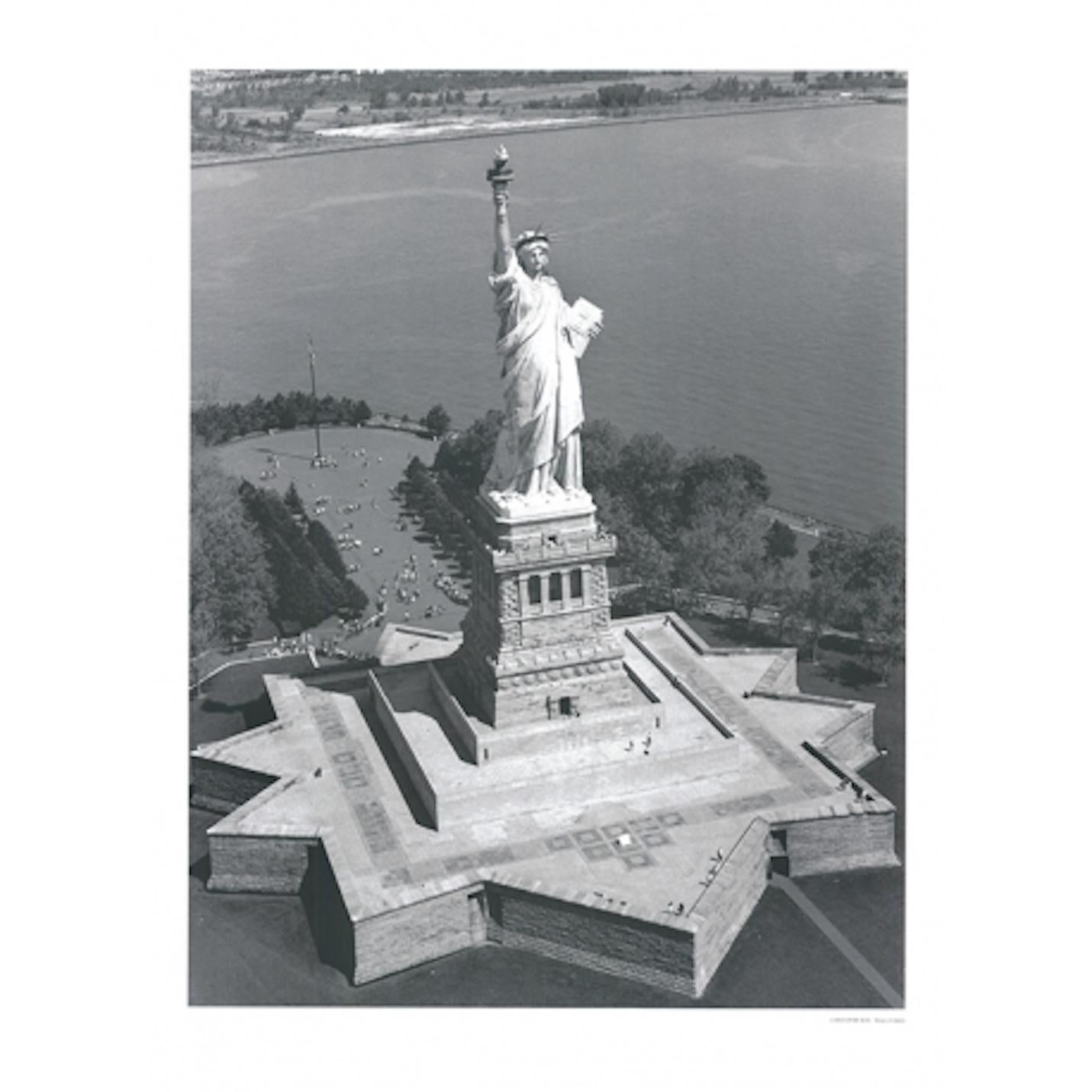 Photographie en noir et blanc qui met en valeur la monumentalité de la Liberté éclairant le monde, la sculpture la plus célèbre des États-Unis est montrée dans le cliché comme une combinaison dynamique de la géométrie du piédestal et de l'organicité