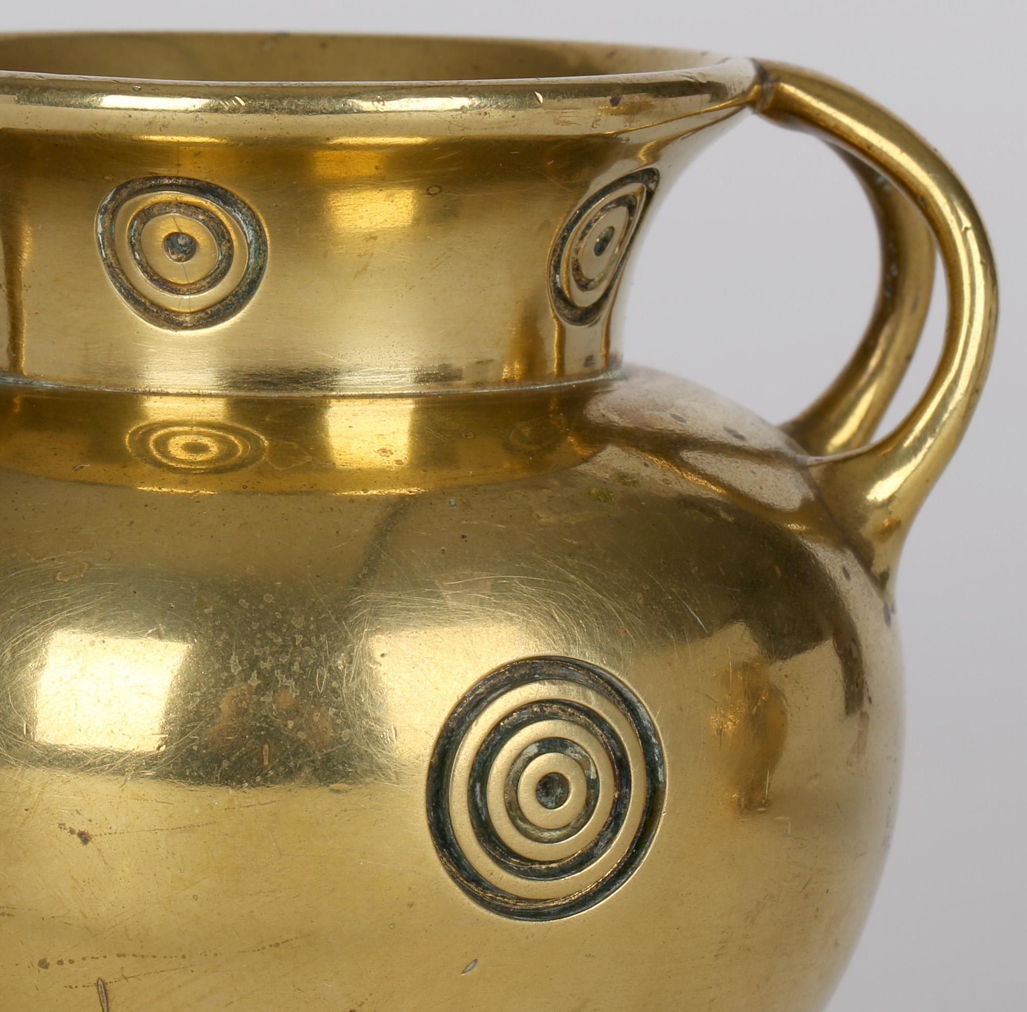 Stylish pair Arts & Crafts Benham & Froud twin handled brass vases with ‘bullseye’ and grooved decoration designed by Christopher Dresser (British, 1834-1904) and dating from around 1885. These heavily made vases art of rounded shape standing on a