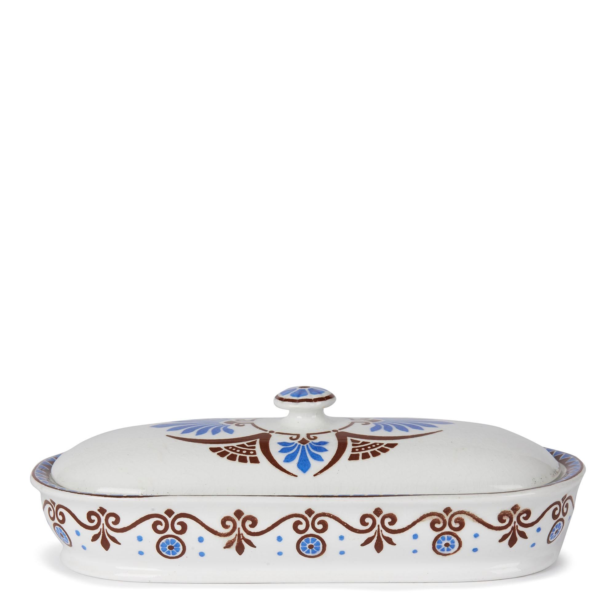 A stylish aesthetic movement Minton pottery bathroom or razor lidded box decorated with a printed design by Christopher Dresser. The long oval ended box has a central domed cover and is decorated in brown and blue printed patterns. The box has
