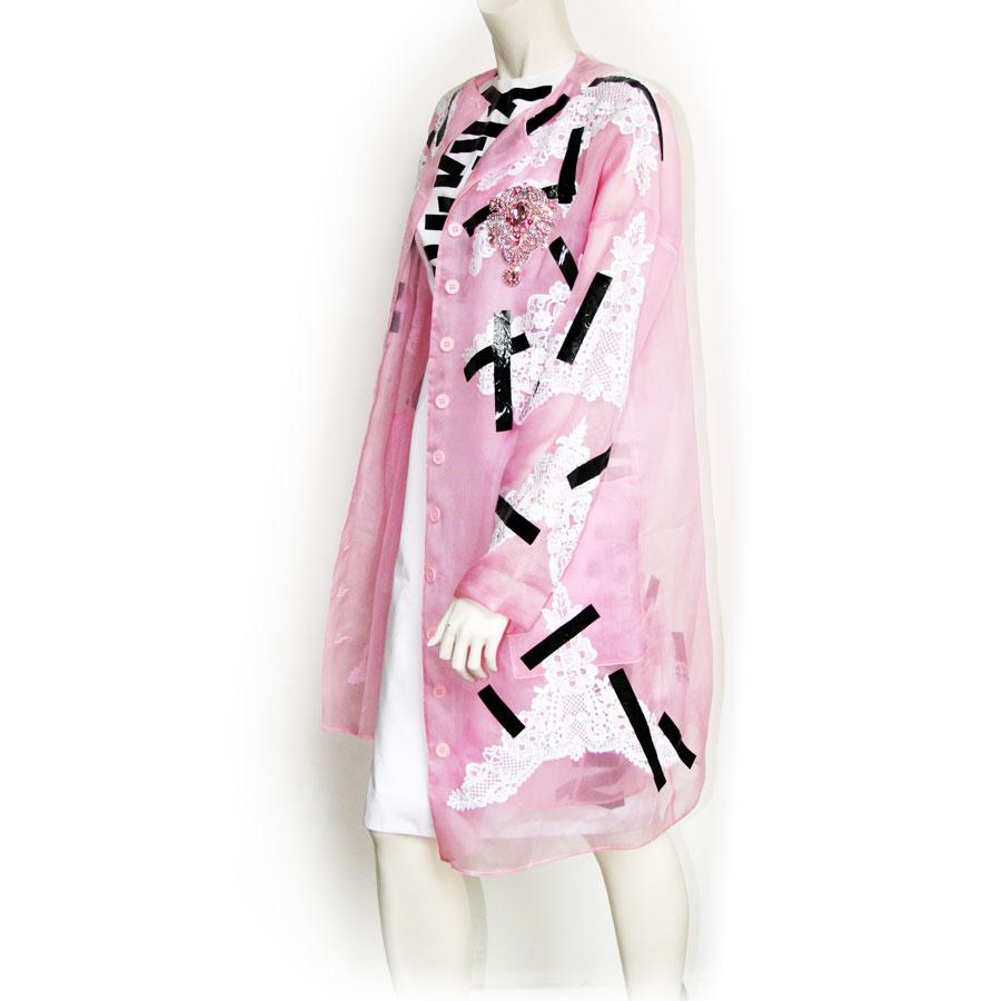 It is a set of long jacket and Christopher Kane dress Size 40. The jacket is in transparent pink silk with white embroidery, a brooch in pink rhinestones as well as pieces of glued tape. The dress is sleeveless white with glued pieces of tape. It