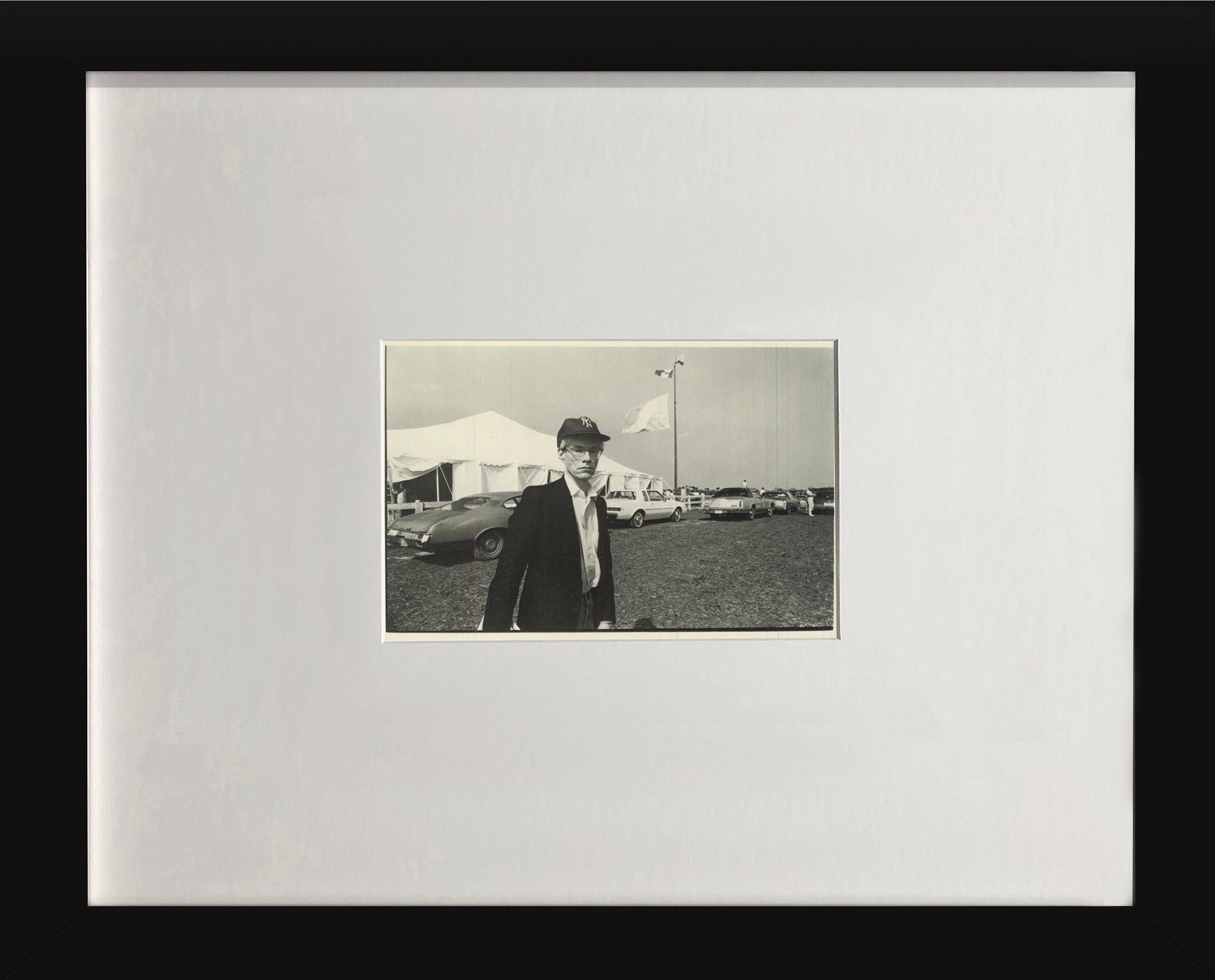 This vintage postcard features a photograph of Andy Warhol by Christopher Makos, capturing the artist passing the press tent at the Palm Beach polo matches in Wellington, Florida, en route to meet Cornelia Guest and Ralph Destino. The image offers a