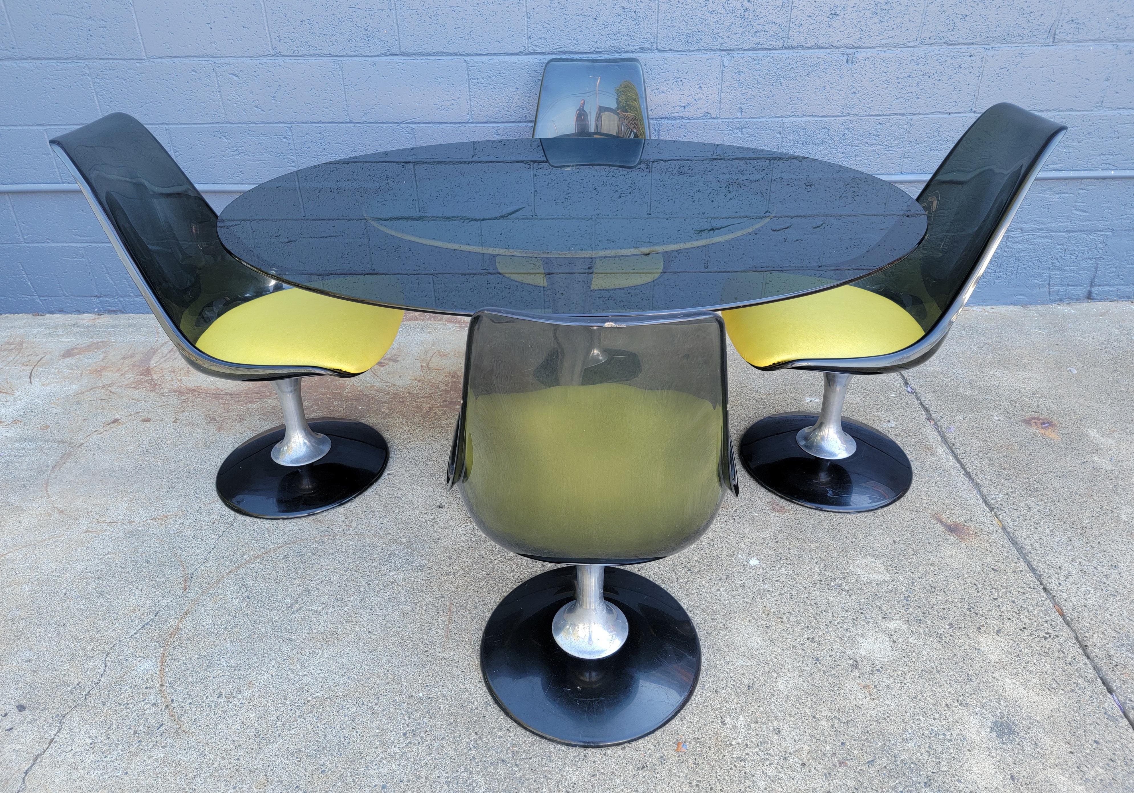 A 5 piece dining or dinette set by Chromcraft, circa. 1970. Set of 4 tulip Base swivel chairs made of aluminum and smokey acrylic. Oval smokey glass table top. Retains 