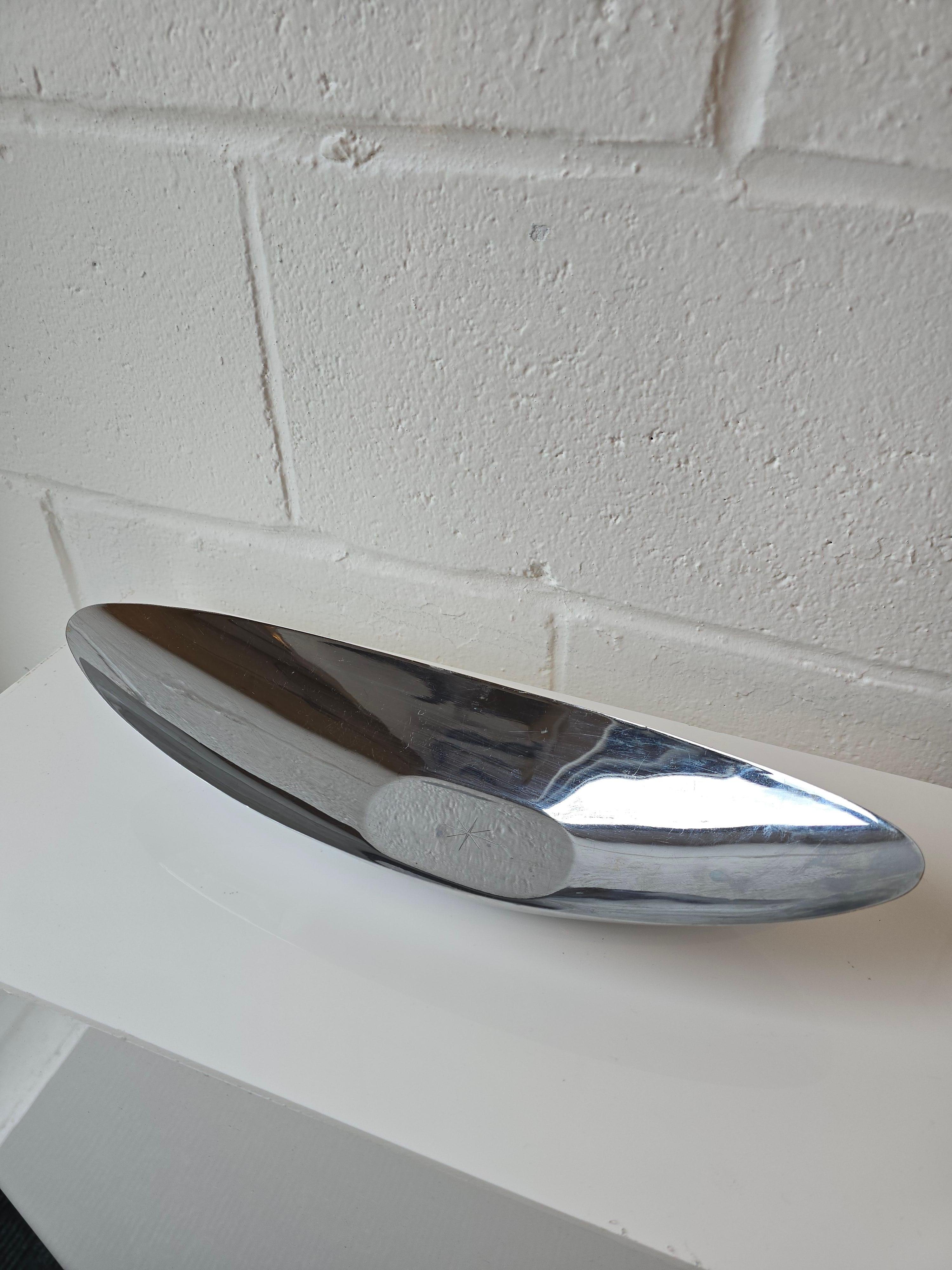 This Japanese-made chrome aluminum decorative bowl features a canoe-shaped design suitable for display or use as a fruit/vegetable bowl or platter.  Its mid-century modern aesthetic, defined by its form and material, is enhanced by a central star