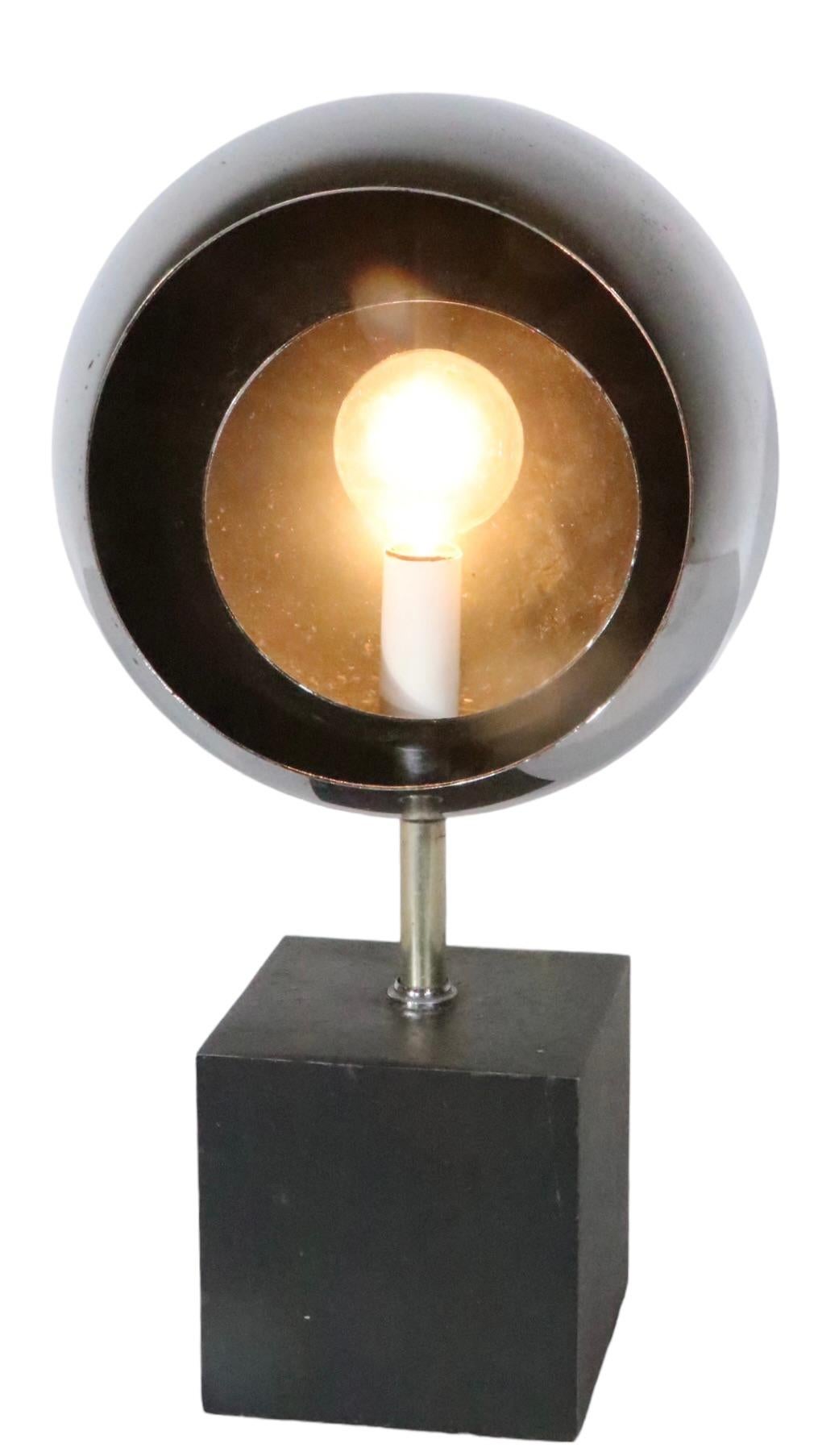 This interesting desk, or table lamp, features a black block form base that supports a chrome ball shade which has a smaller chrome ball inside it, that rotates to control the light. The lamps in original and working condition, it does show  wear to