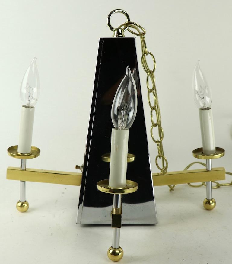 Interesting architectural modernist chandelier having a chrome pyramid form body with discrete interior downlight bulb, and four brass candle arm side lights. This fixture was originally installed as a swag light, popular circa 1970s, but can be