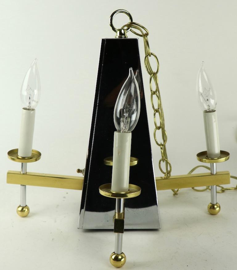Interessante lampadario architettonico modernista con corpo cromato a forma di piramide, lampadina interna discreta e quattro luci laterali in ottone a braccio di candela. Questo apparecchio è stato originariamente installato come lampada a fascia,
