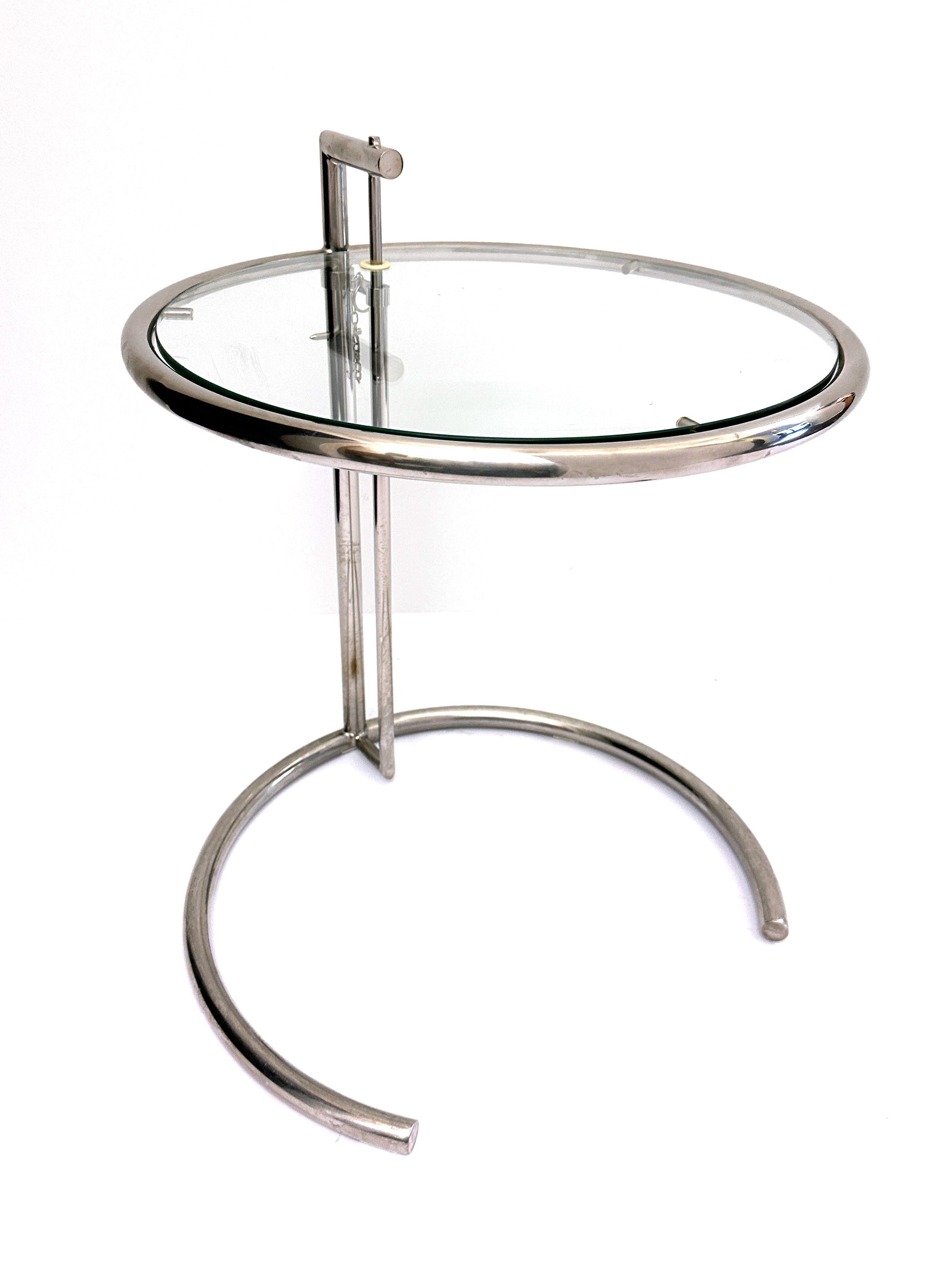 A chrome and glass accent table attributed to the E-1027 design by Eileen Gray. This elegant and well designed piece has an adjustable top that can be moved vertically to fit multiple table top heights. The table has a clear glass top with silver