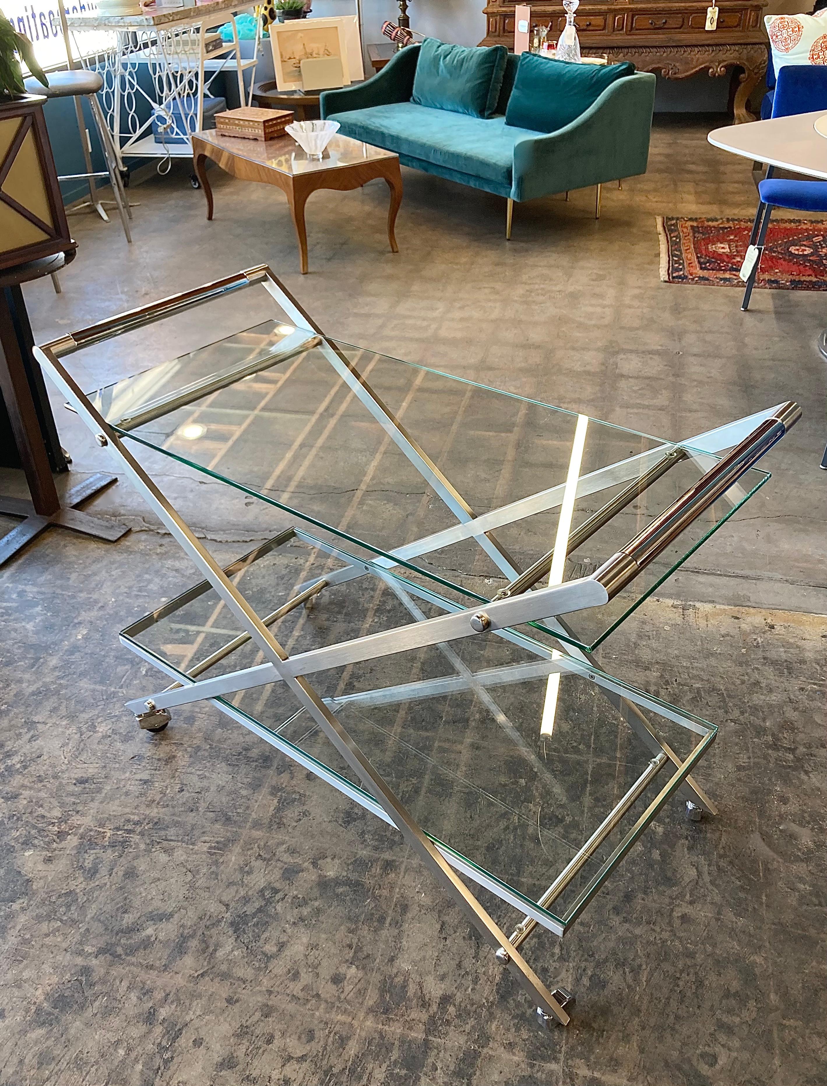 1970's/80's X-frame rolling bar cart, with two glass shelves. Classic mid-century futuristic style with brushed steel and chrome accents. Wheels fully swivel and metal is in fantastic vintage condition. Glass has minor scratches and are pictured
