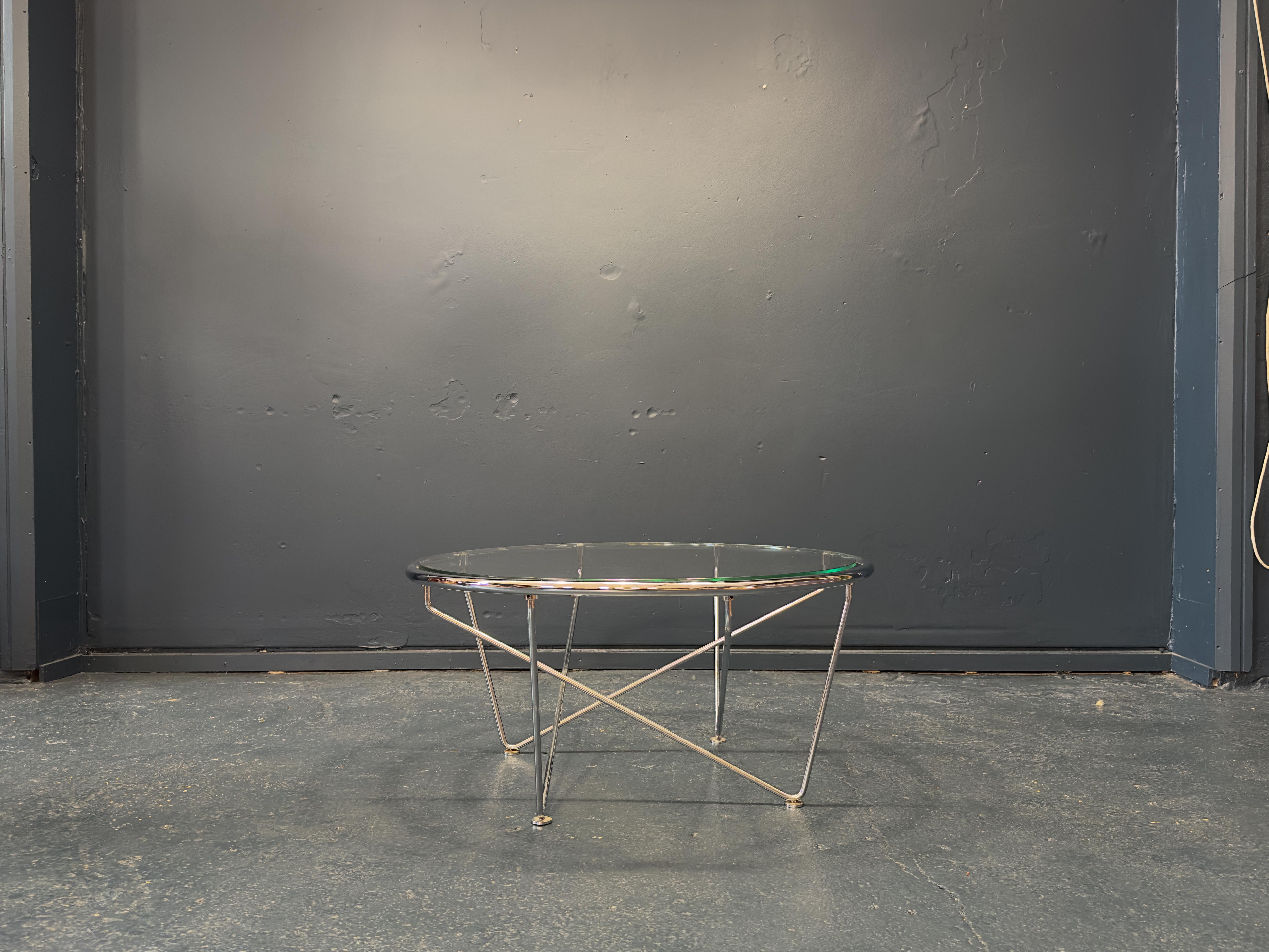 This coffee table features a round glass removable top on a chrome frame. Strong lines and angular shapes create the legs of the chrome frame, the choice of glass as the tabletop creates a sleek and statement feel to the piece as the angles created
