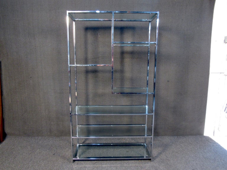 A stunning chrome and glass etagere in the style of Milo Baughman from the mid-century modern era. Features six shelves, four full-width and two half-width. In great condition, a truly beautiful piece to own. Please confirm item location (NY or NJ.)