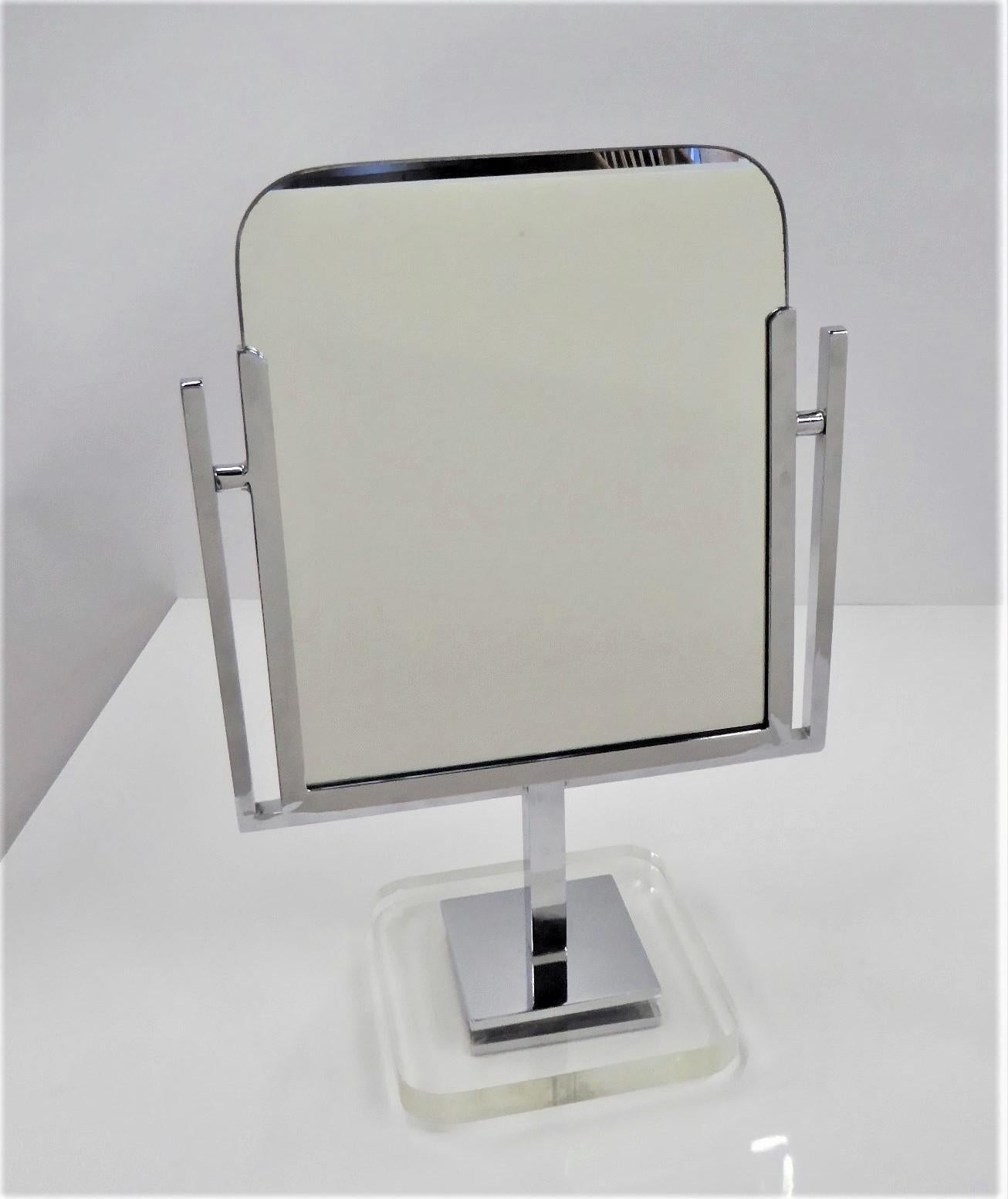 A double-sided Vanity mirror framed in chrome and standing on a lucite base. The mirror is designed to tilt back and forth. The Lucite base is 6 7/8 inches square with rounded corners. The overall height is 17 3/4 inches x 12 inches wide.

Charles
