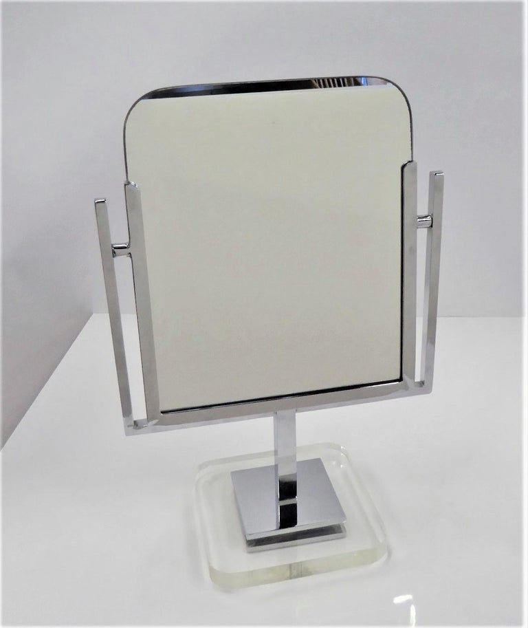 A double-sided Vanity mirror framed in chrome and standing on a lucite base. The mirror is designed to tilt back and forth. The Lucite base is 6 7/8 inches square with rounded corners. The overall height is 17 3/4 inches x 12 inches wide.

Charles