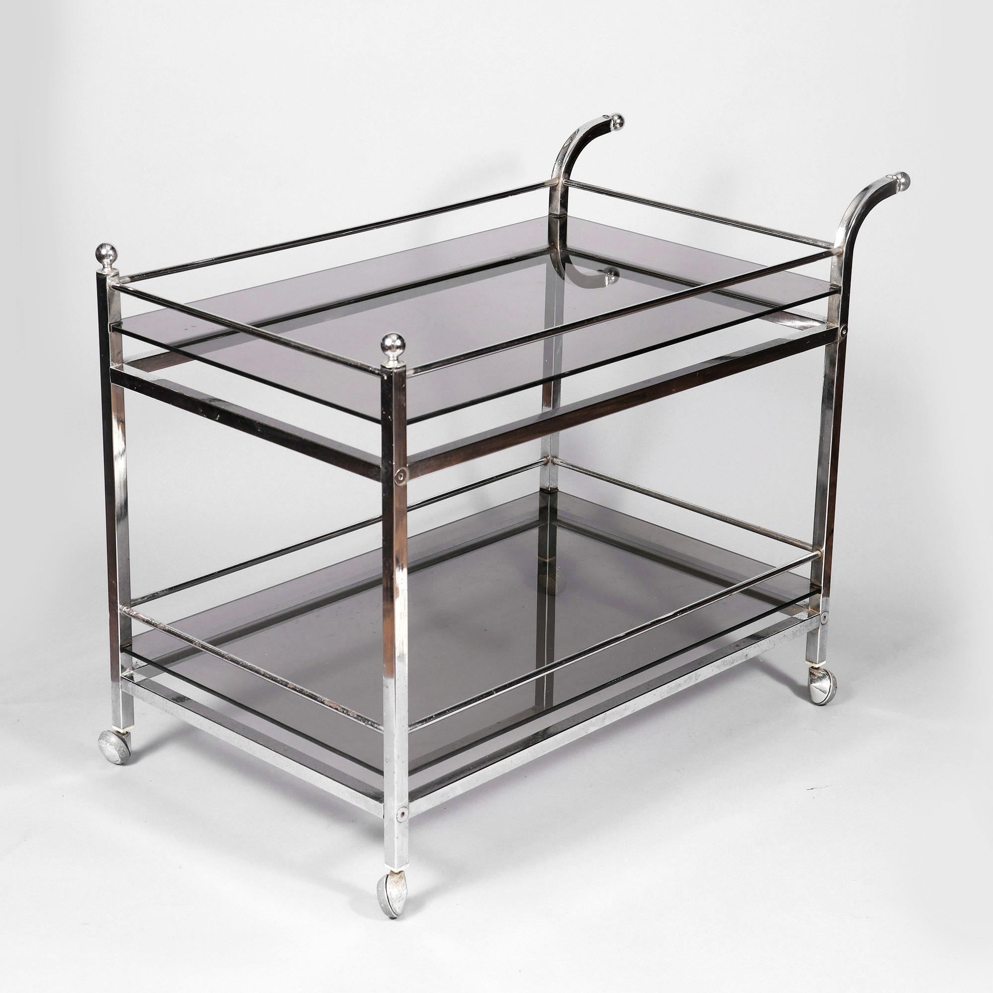 A chrome drinks trolley with smoked glass tops fashioned from square tubed legs and cross bars fixed with flush circular bolts. The trolley with ball finals to the front legs and fitted to the ends of curved tube handles. The whole is on four