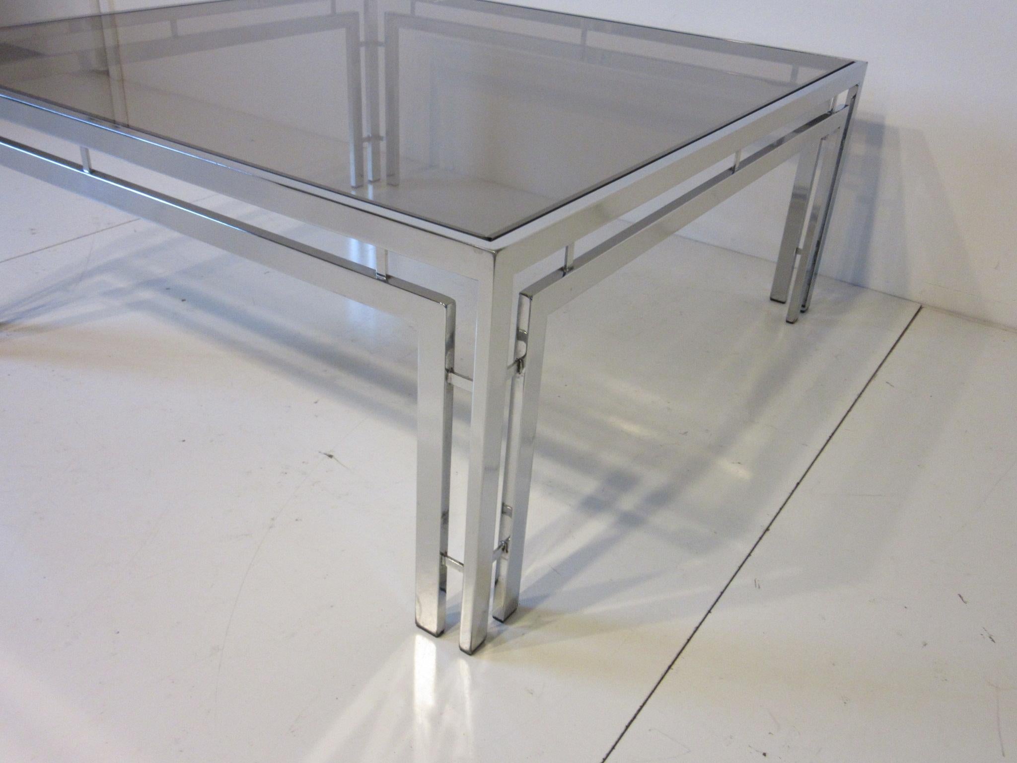 A chromed coffee table with medium smoked glass top and detailed support structure, in the manner of Milo Baughman.
