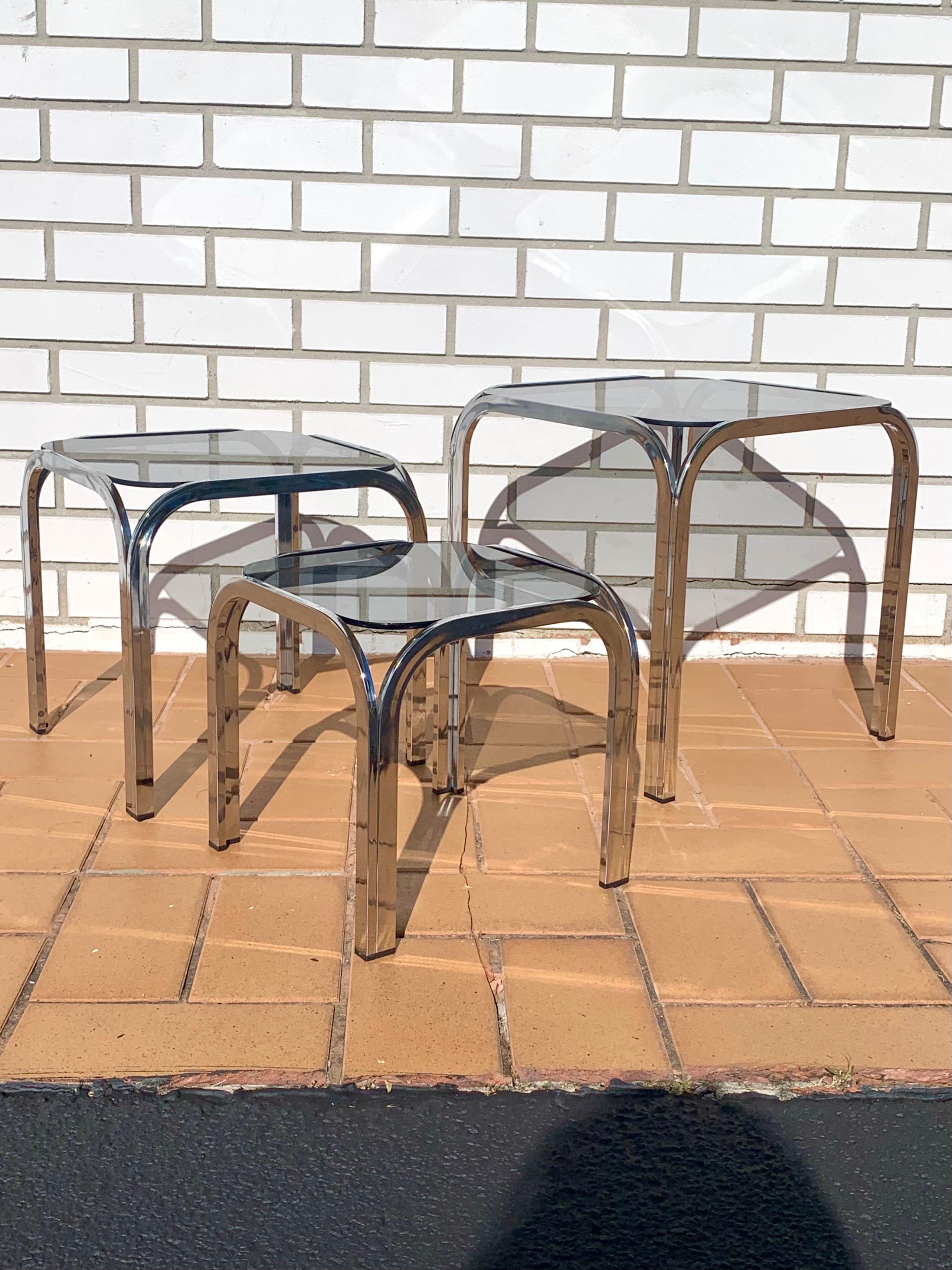 Set of 3 chrome nesting tables. With smoked glass. Simple yet elegant archway design. Each smaller table fits under the next bigger table. Tables are in great condition with no damage to the chrome and only some light scratching on the glass.