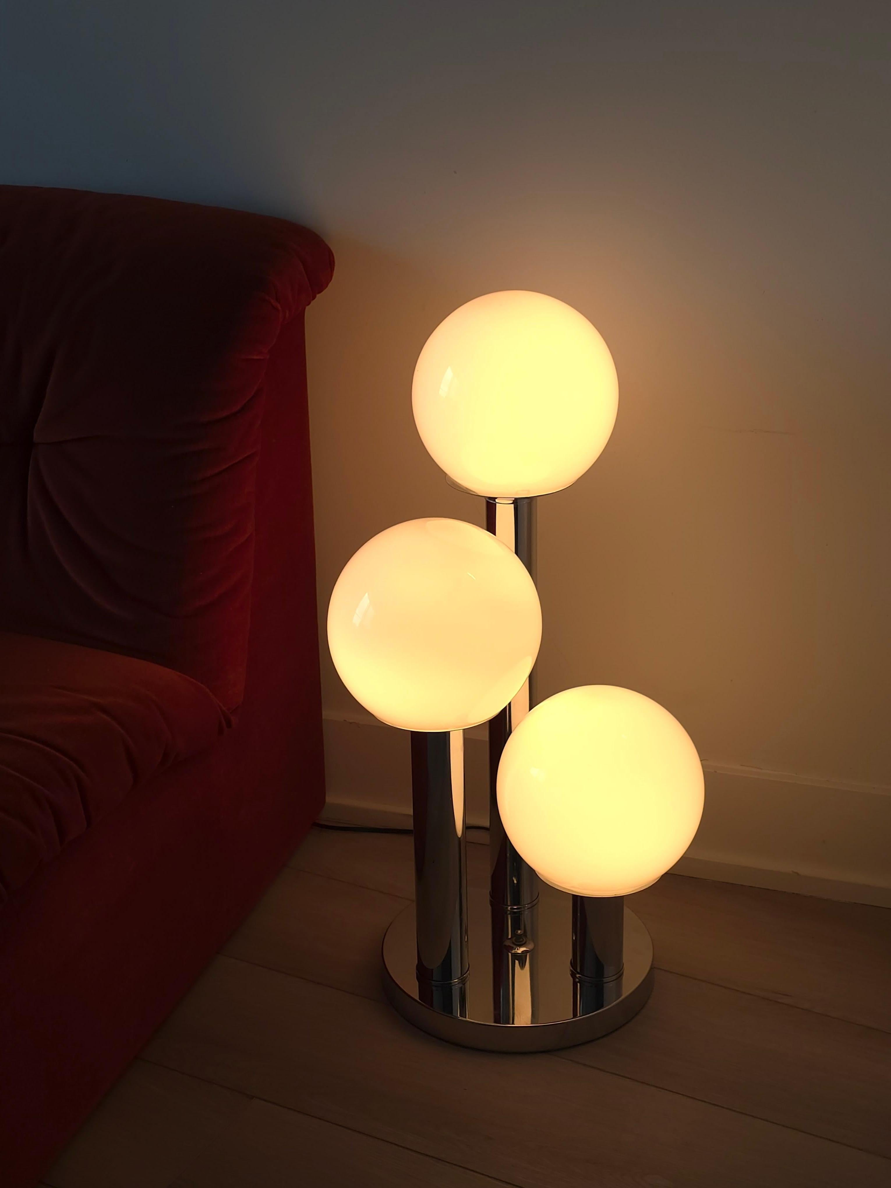 Stunning glass globe and chrome table lamp. This lovely lamp has three cylindrical tiers in varying heights that are connected at the chrome base featuring three glass globes. The white milk glass globes cover the light bulbs. The glass globes are
