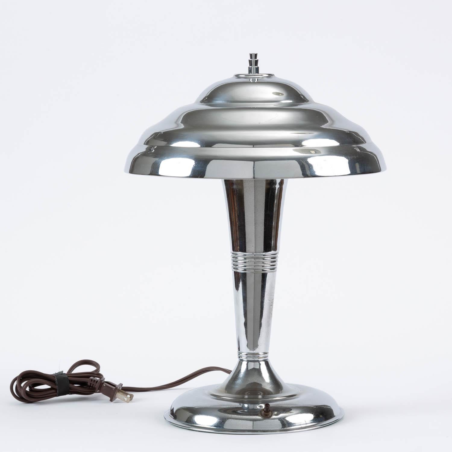An Atomic Age / Art Deco table or desk lamp with an attached saucer shade made from chrome-plated spun steel. Lamp has been professional rewired.

Condition: Good vintage condition; professionally cleaned and rewired. Some pitting on
