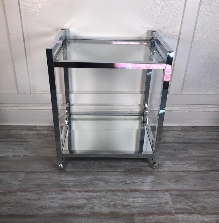 Milo Baughman style chrome, glass, and mirror bar cart, 1970s two-tier with upper clear glass shelf and lower mirrored shelf. On castors. Few scratches to glass and mirror from age and use.