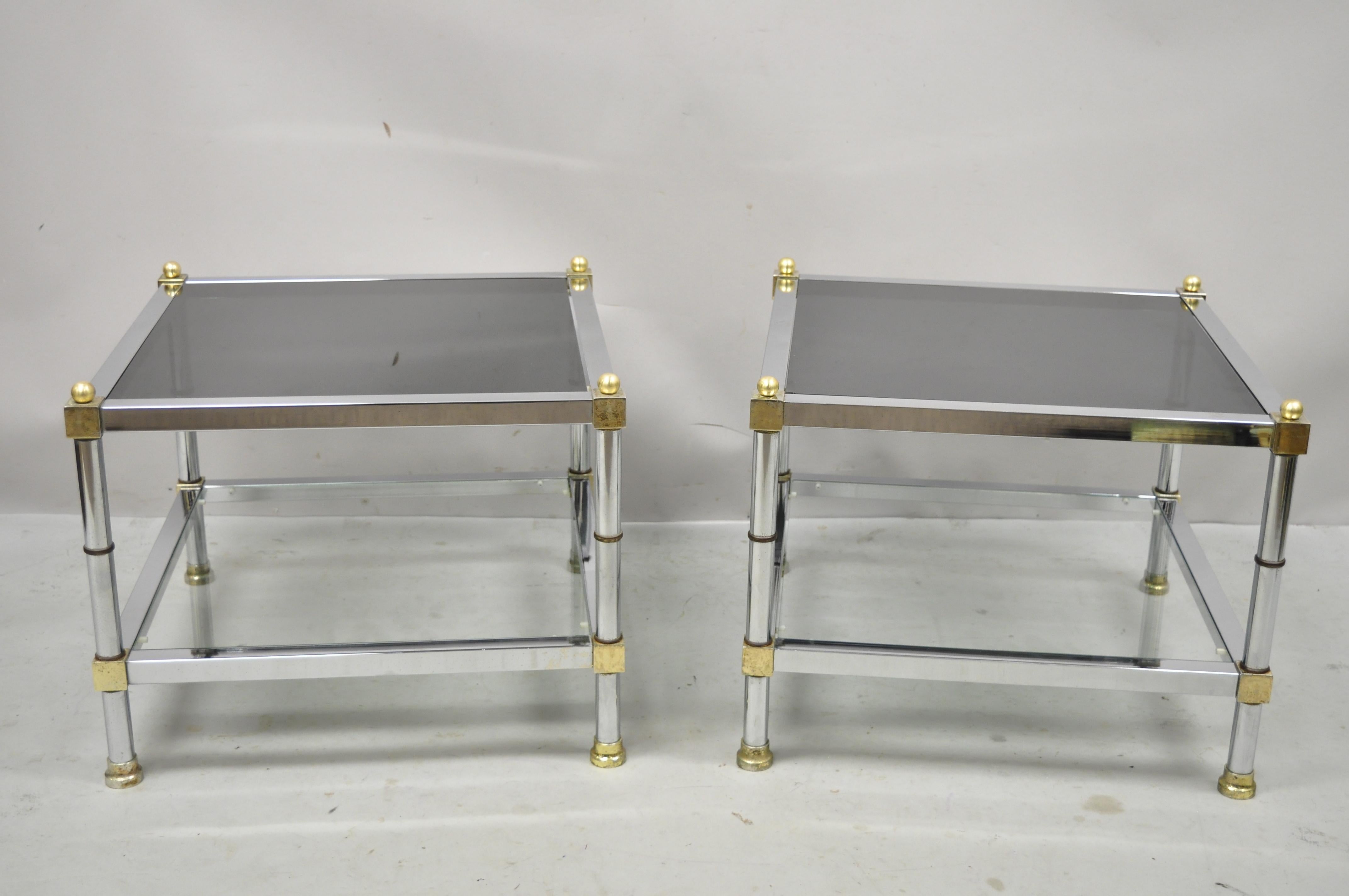 Vintage chrome and brass Maison Jansen style Hollywood Regency square glass top end tables - a Pair. Item features smoked glass top, clear glass lower tier, square chrome frame, brass accents, great style and form. Circa 1970s. Measurements: 16.5