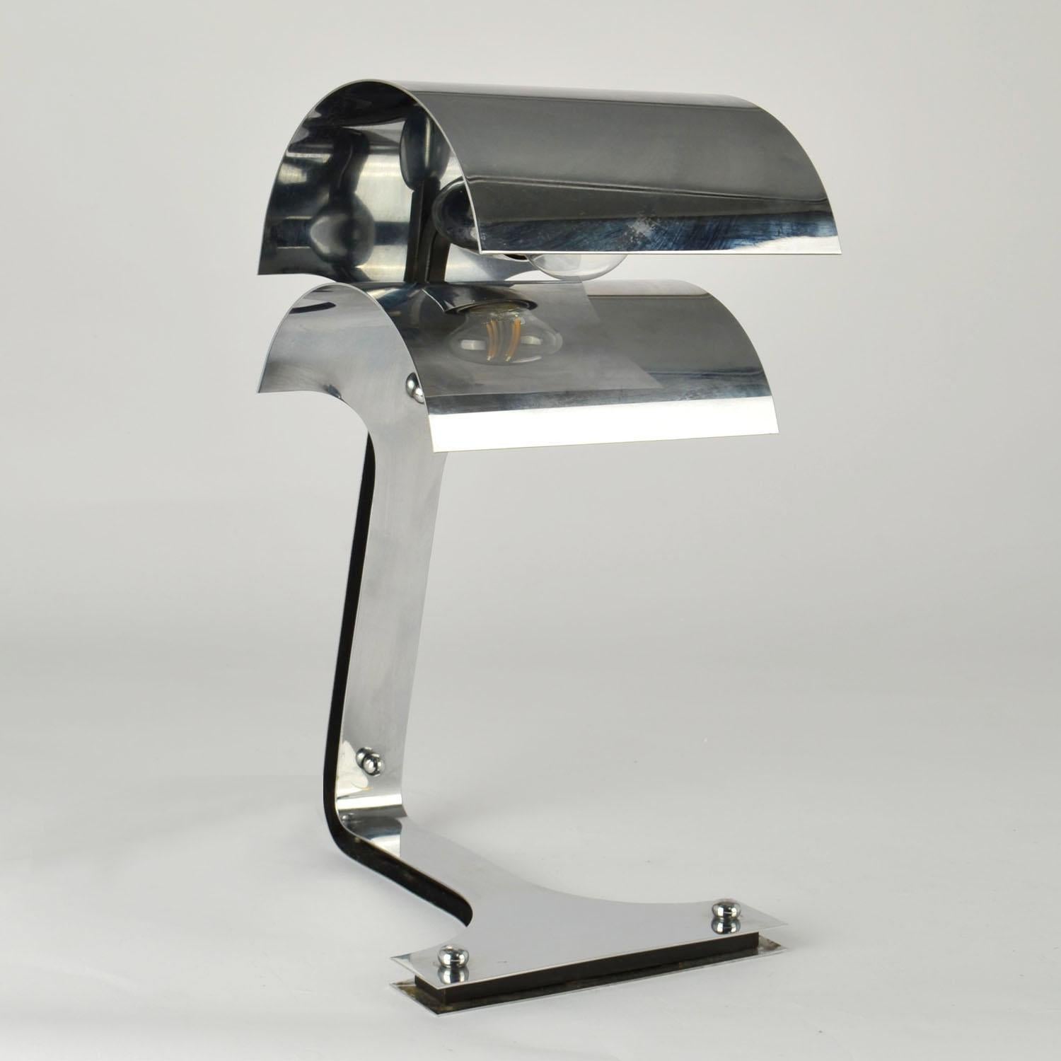 Sculptural chrome table or  desk lamp  Italy 1960's is very avantgarde in its design. The foot curves into a double shade that works as a diffuser to hide the bulb and directs the light downwards on to the table. Designers like Joe Columbo, Reggiani