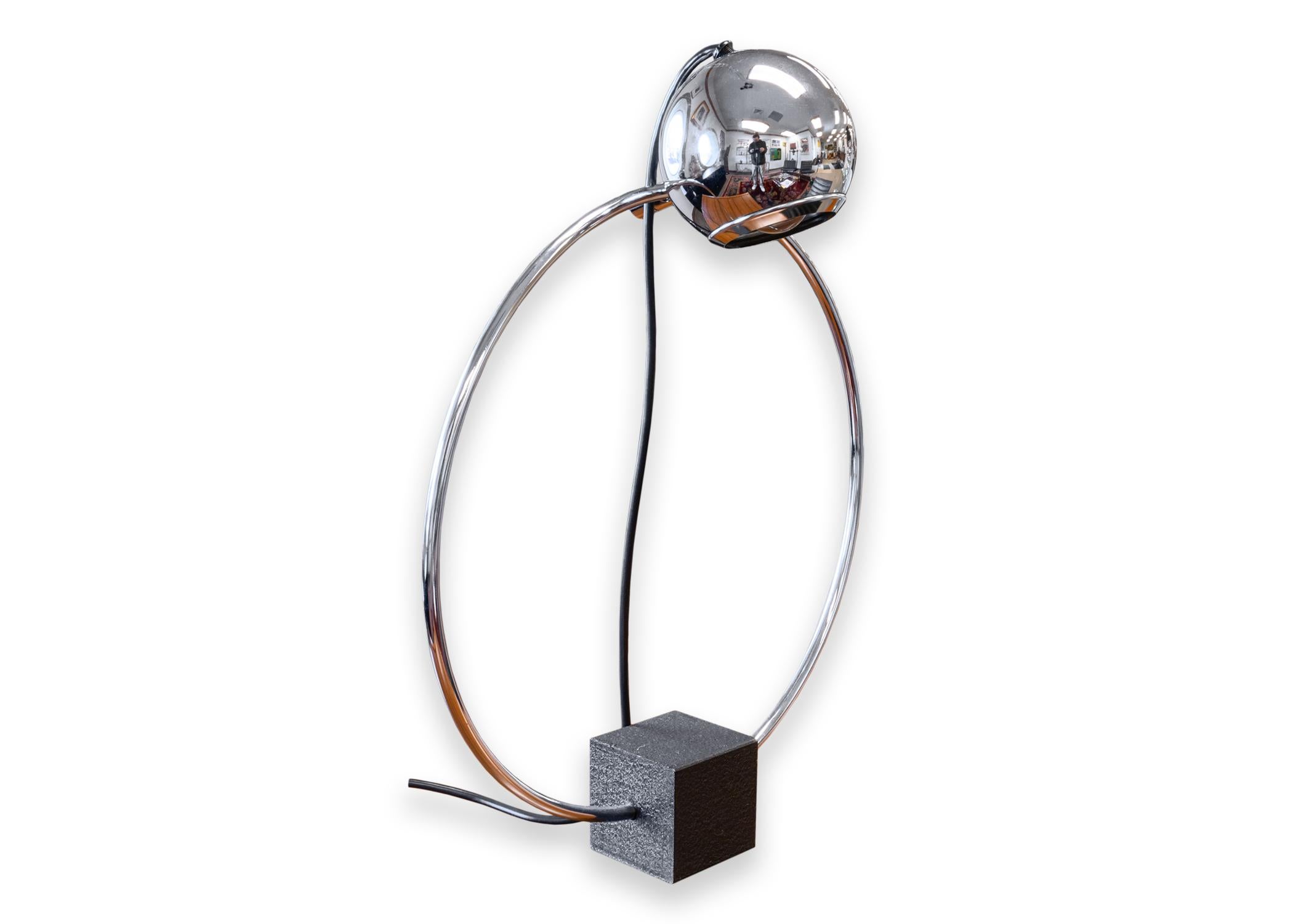 An eyeball atomic orbiter table lamp circa 1970. This is a lovely mid century modern table lamp featuring a chrome plated design, and a black square base. This lamp is very adjustable. The lamp head tilts, turns, and shifts all around the round