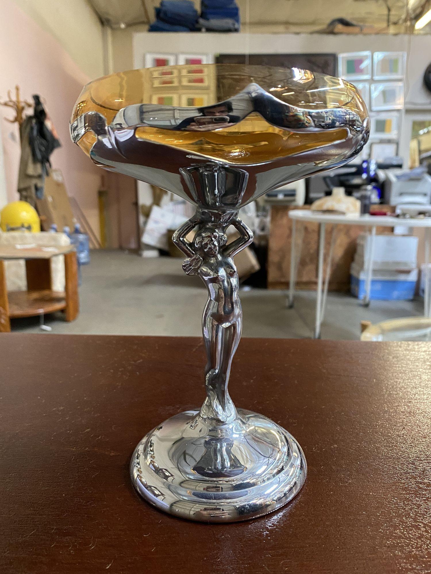 Vintage Farberware compote featuring a chrome stem with a nude woman having a Cambridge insert from 1932. The compote features a nude women standing on a stepped round base holding up an amber glass cup insert.

The compote is 7 ¾ inches tall, the