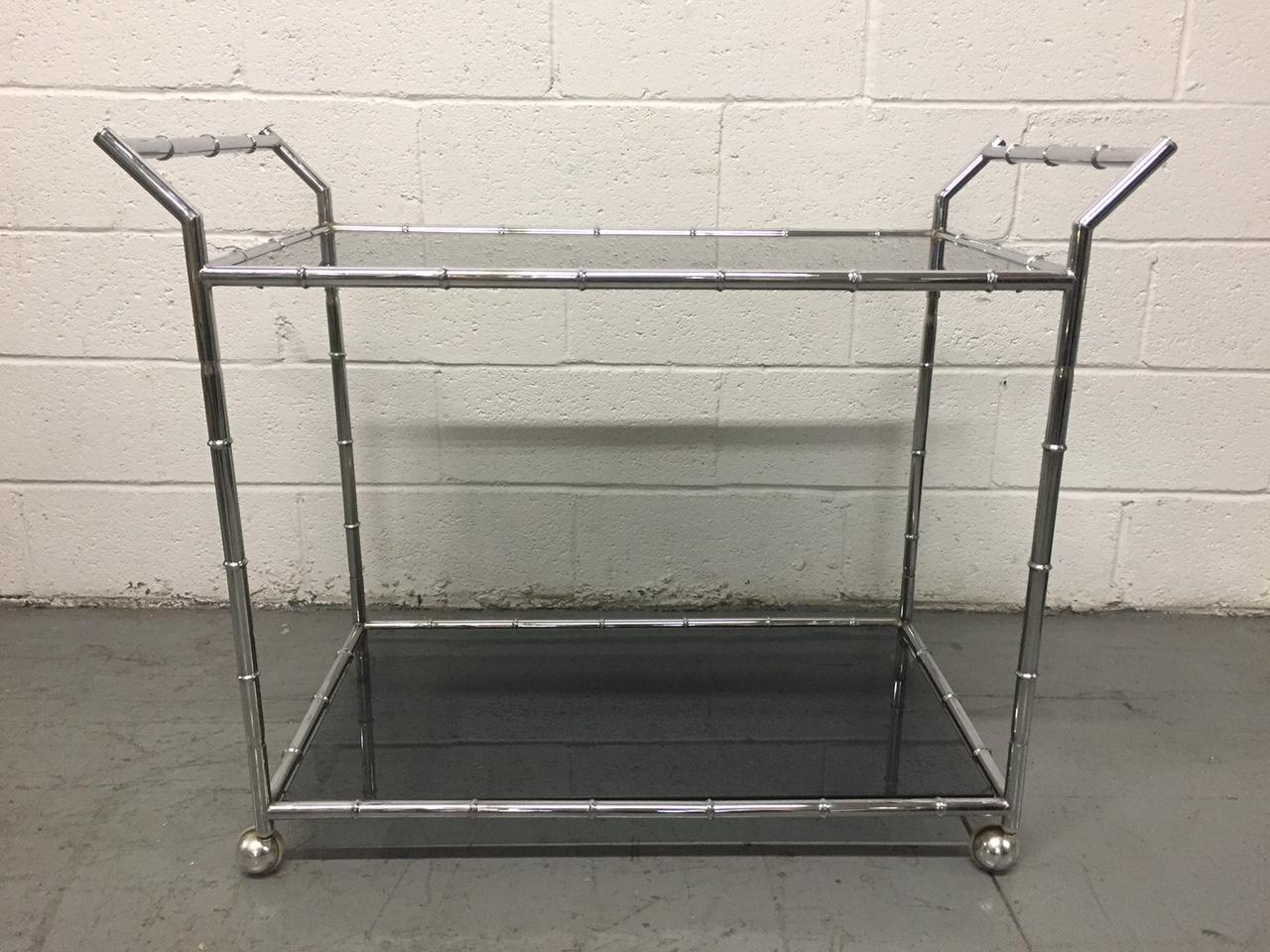Two-tier bar or serving cart, smoked glass tops with a chrome faux bamboo frame.
