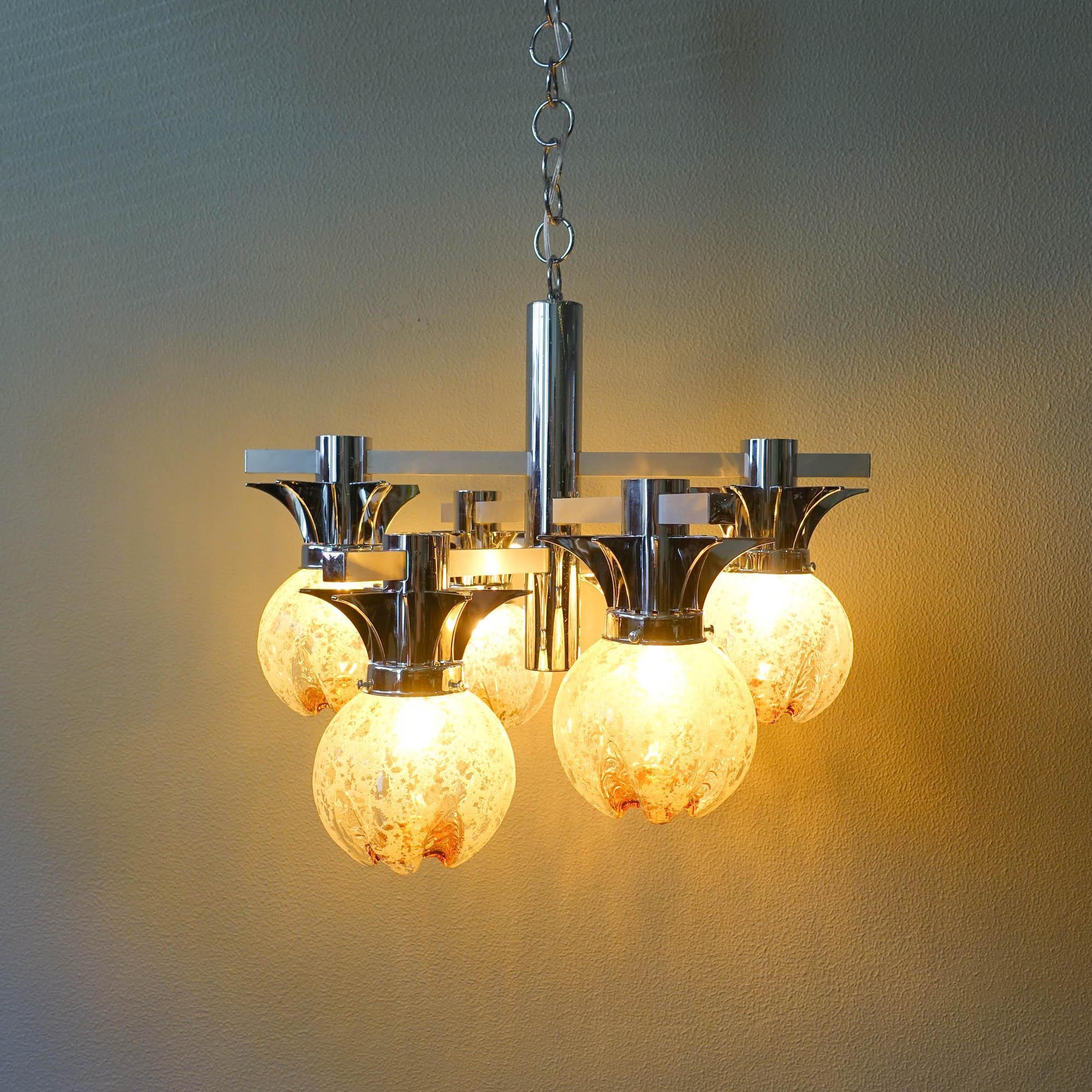 This pendant lamp was designed by Gaetano Sciolari for Mazzega, in Italy, during 1970's. It features six arms in an asymmetric chromed metal frame. In each arm is a murano glass globe that goes from transparent white to orange-amber gold glass.