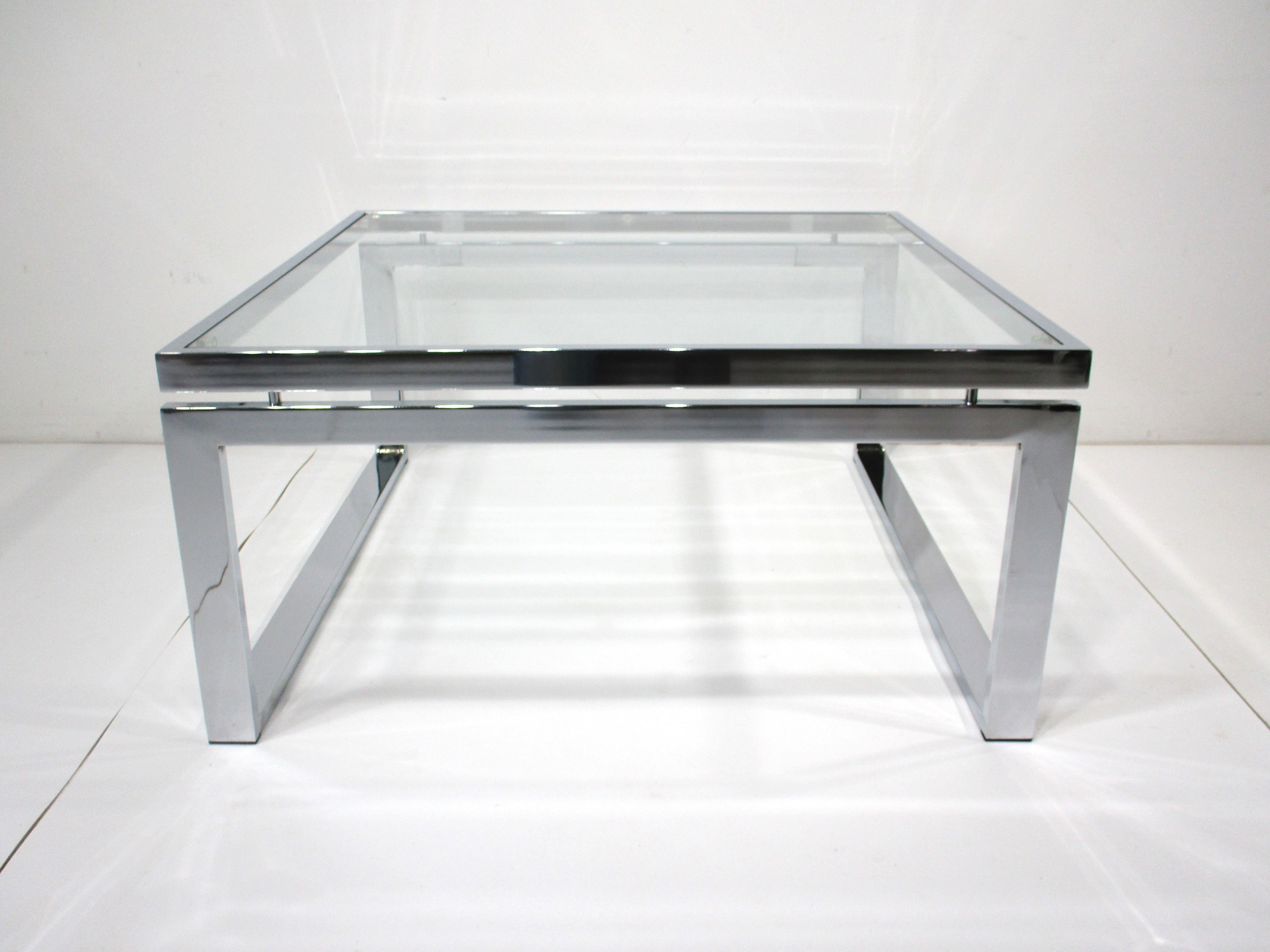 A chromed metal flat bar coffee table with floating top section having a glass top . A very clean sophisticated form in the perfect size for that living room , entertainment area or sitting room . Designed in the manner of Milo Baughman .  