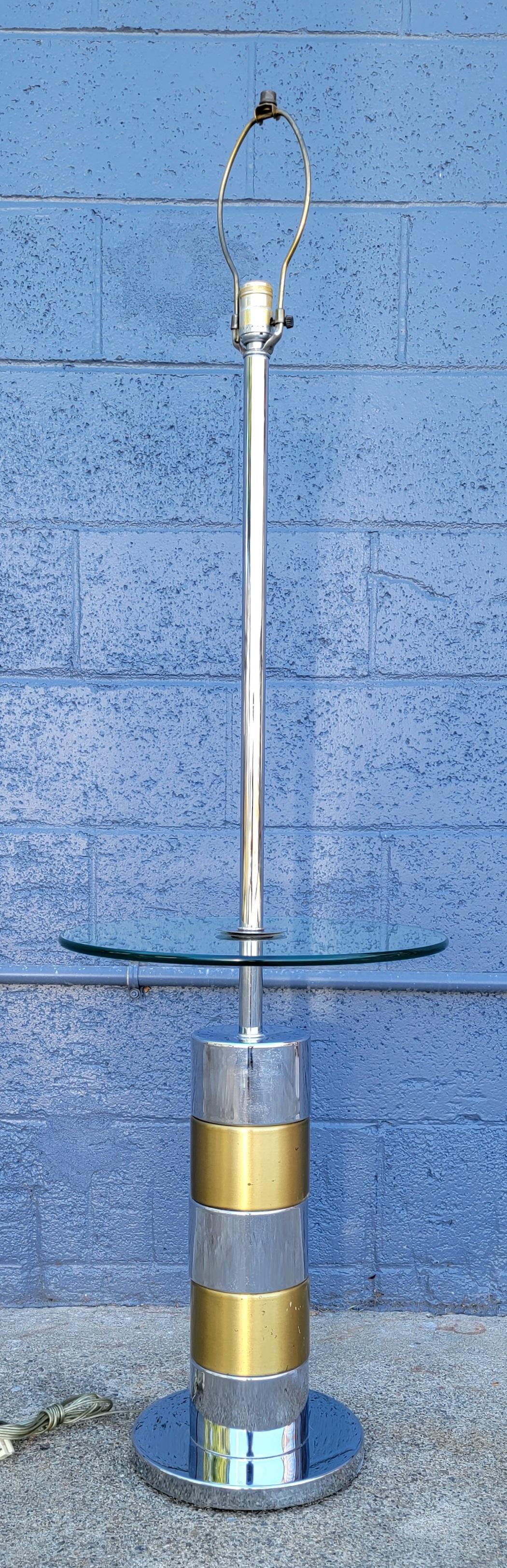 A polished chrome and brass floor lamp with a circular glass table top. Designed in the manner of Paul Evans. Circa. 1970's. No lamp shade. Glass table top measures 22.25