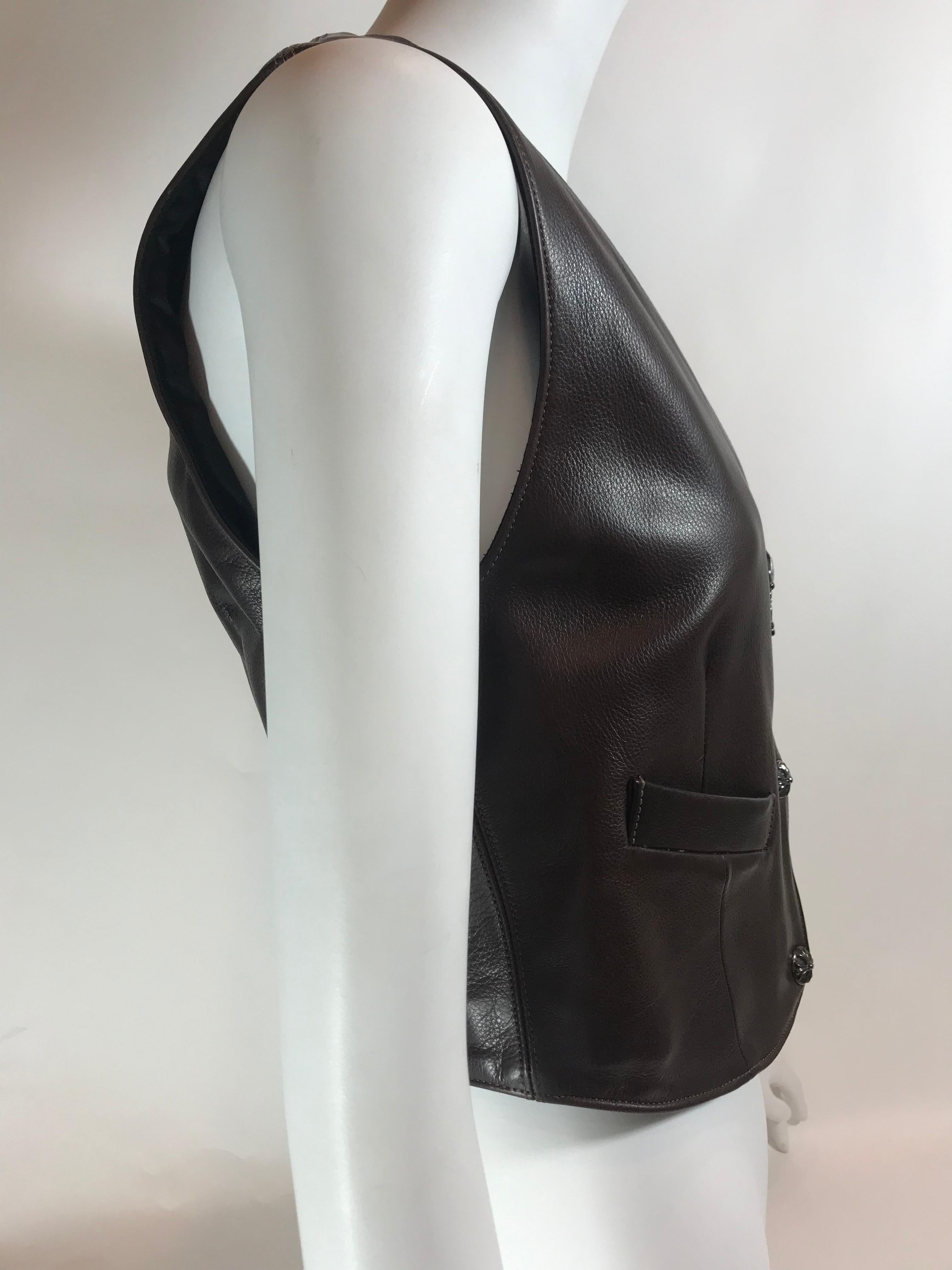 Brown leather. Silver-tone hardware. Zip up closure at front. V-neck. Lined interior. Embellished and embroidered design at back with small belt buckle design.