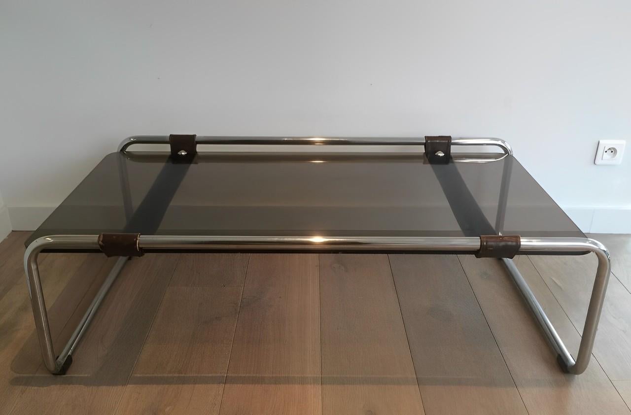 Esta mesa de centro, rara y muy inusual, está formada por una base cromada con una ancha banda de cuero y una tapa de cristal ahumado. Se trata de una Obra francesa al estilo del famoso diseñador Jacques Adnet. Alrededor de 1950