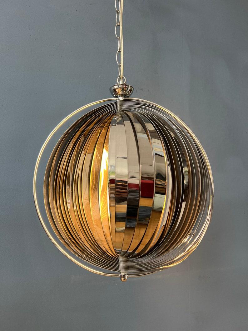 Remake rétro de la suspension 'lune' de Henri Mathieu et Panton. La lumière se reflète magnifiquement sur les parties chromées. La lampe nécessite une ampoule E27/26 (standard).

Informations complémentaires :
Matériaux :  Métal, bois
Période :