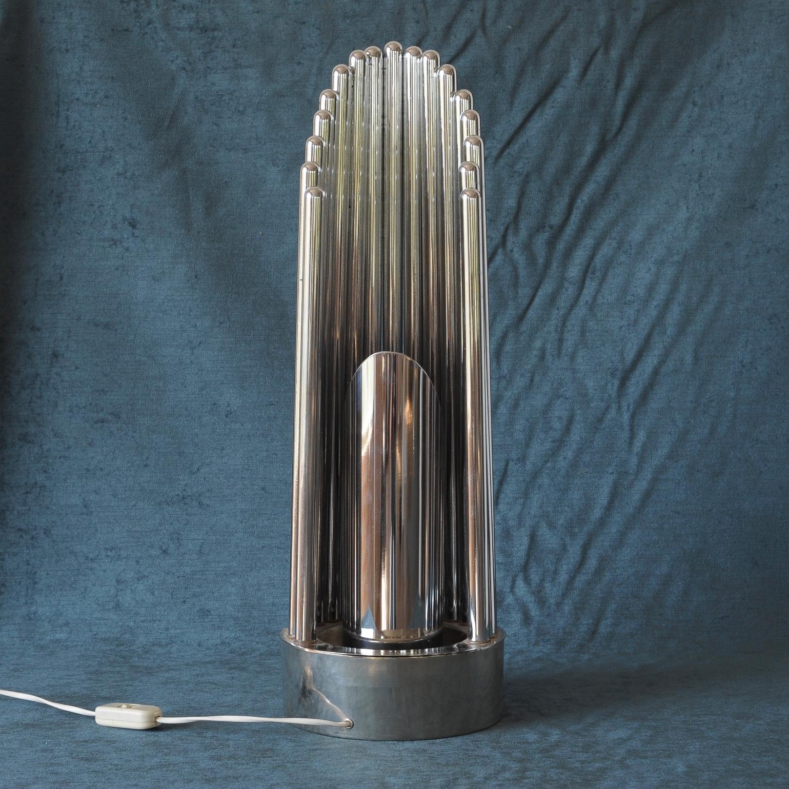 Chrome table lamp of tubular pipes on a strong platform base.
Rotating tube with light source in the middle of surrounding banister of chromed pipes.
 