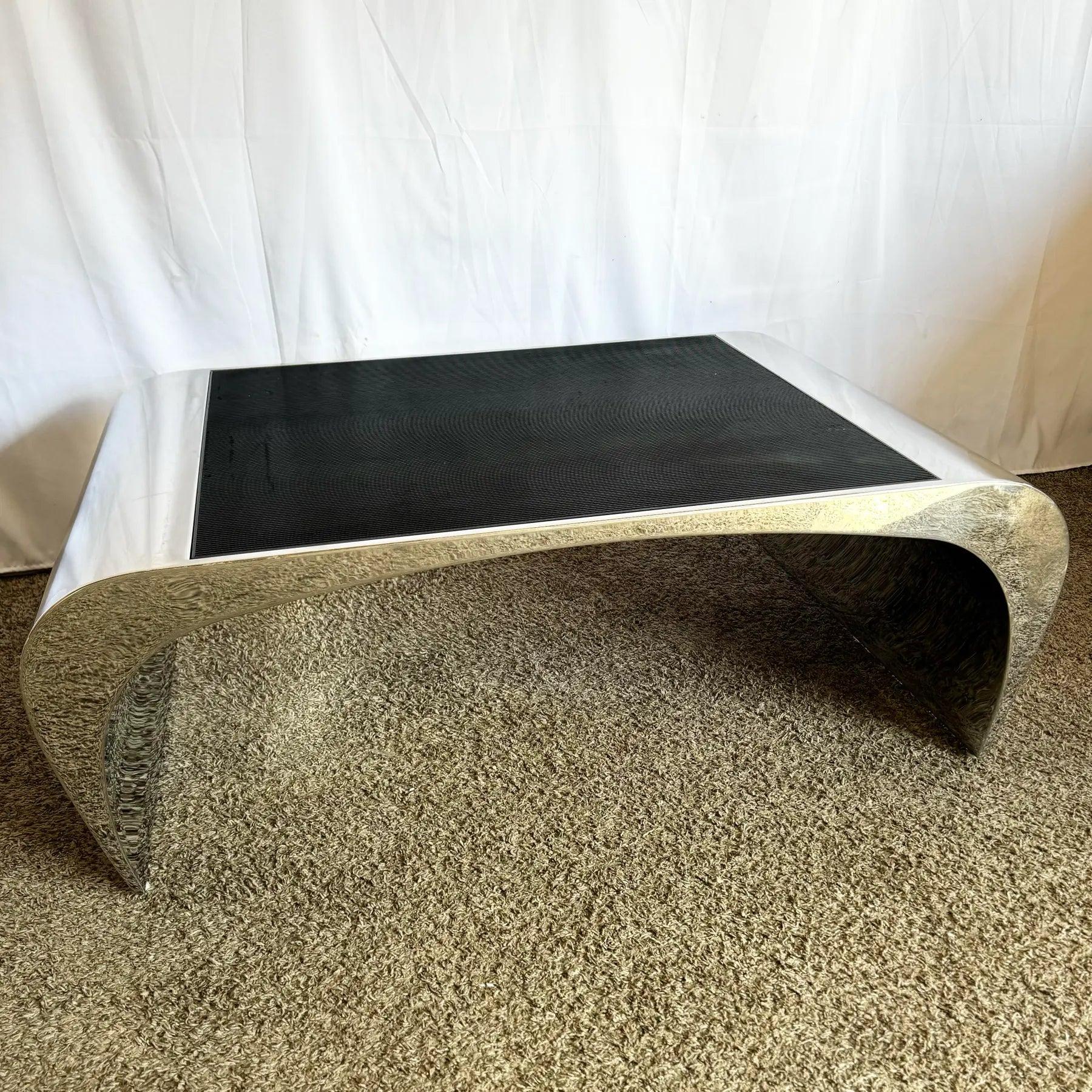 Table basse cascade épurée en acier poli chromé avec des courbes fluides et un plateau en grille métallique inséré, parfaite pour les intérieurs modernes ou postmodernes.
 
 Quelques usures de surface et rayures au niveau du polissage comme on peut