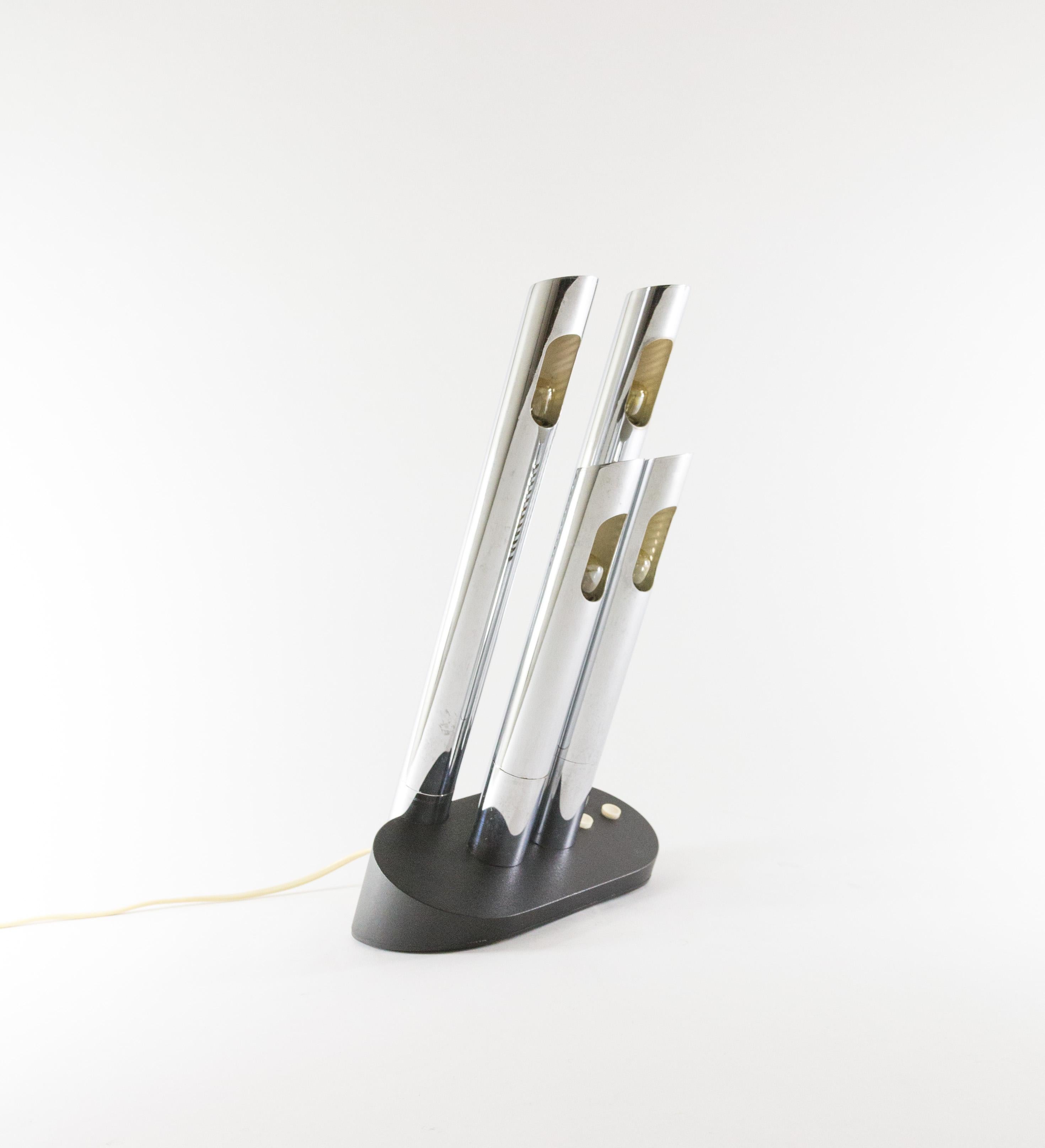 Lámpara de sobremesa modelo T443 de metal con cuatro tubos cromados, diseñada por Mario Faggian para el fabricante italiano Luci Illuminazione en la década de 1970.

El modelo tiene cuatro fuentes de luz y dos interruptores, uno para los tubos