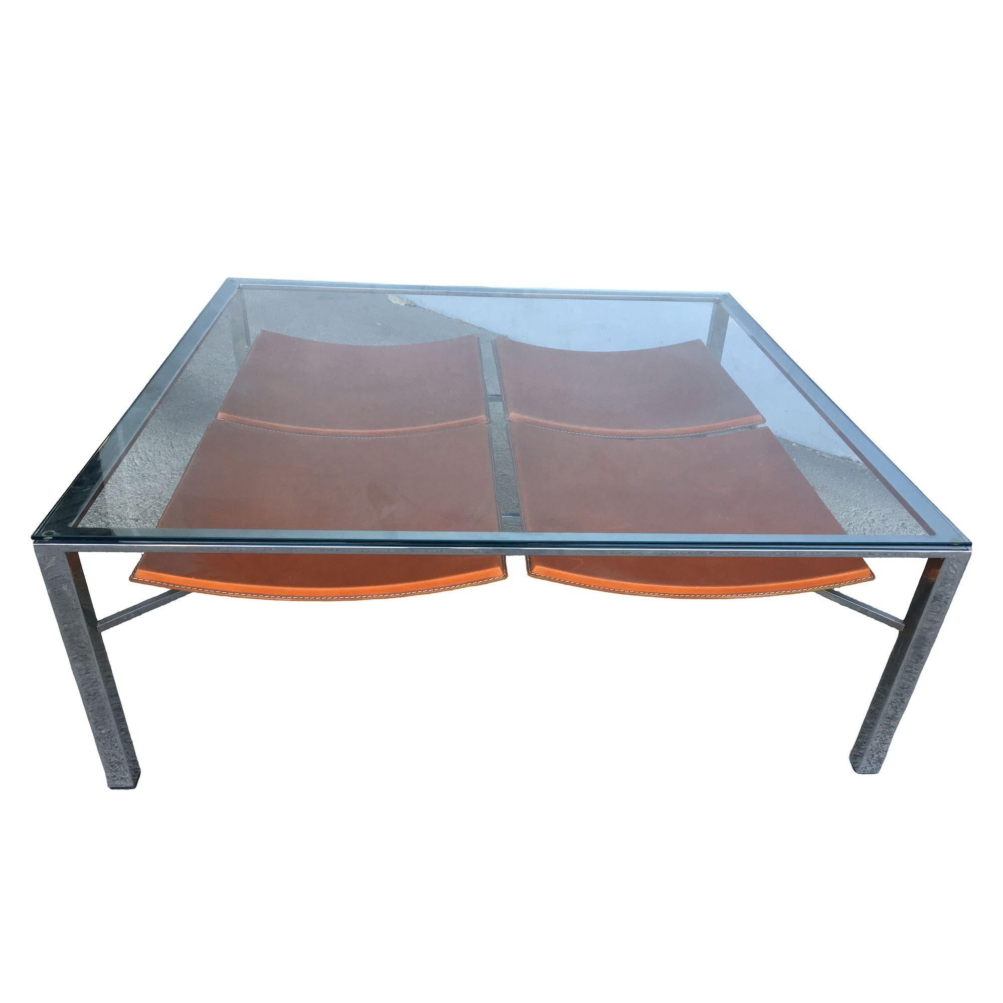 Table basse postmoderne à plateau en verre tubulaire chromé, dotée d'un cadre minimaliste élégant et de porte-revues intégrés en cuir. Le cuir cognac chaud contraste magnifiquement avec le chrome industriel froid, tandis que le plateau en verre