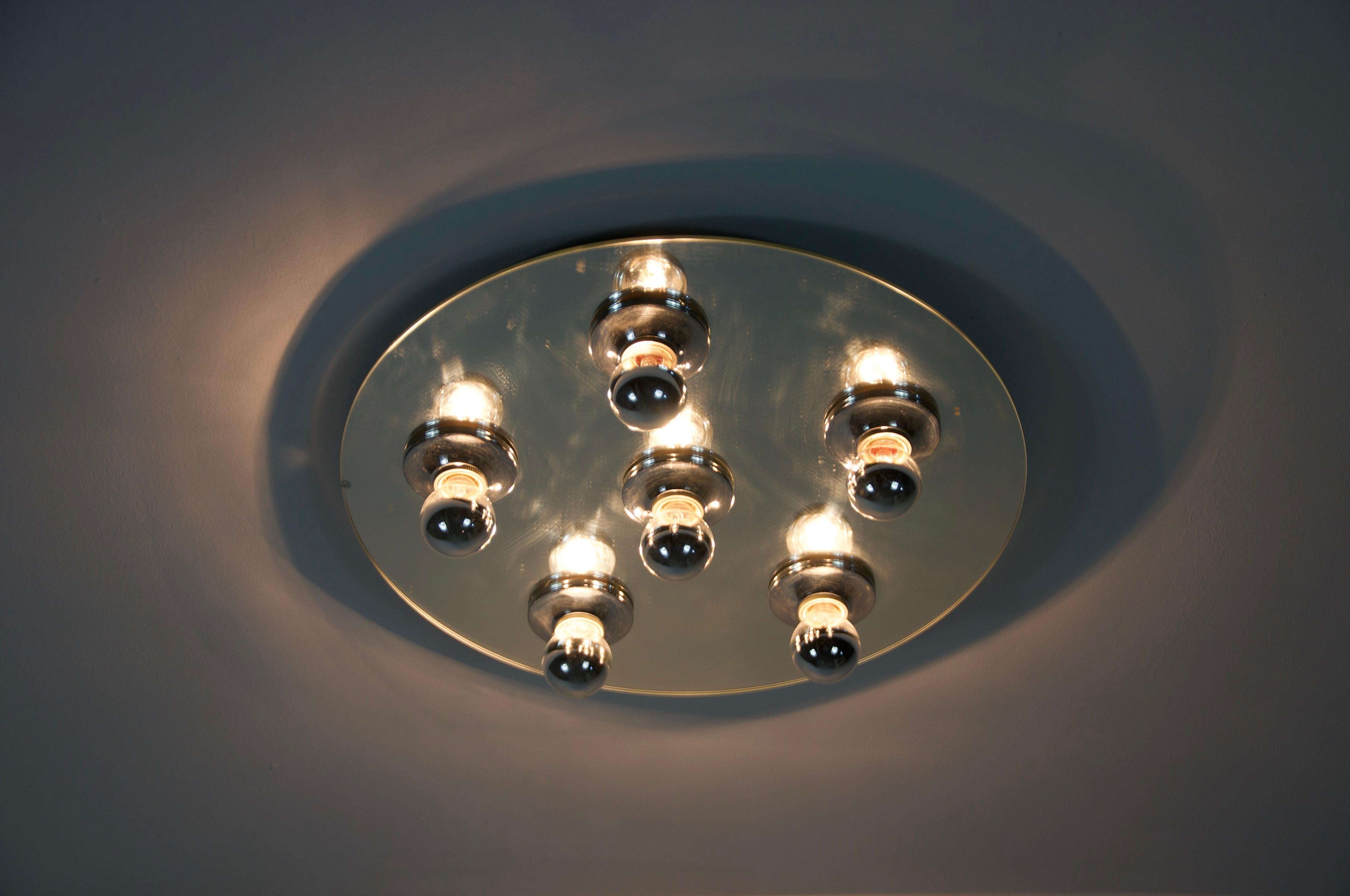 This unique ceiling lamp from the 1970s features a striking round design with a chrome finish and a mirrored surface, creating a sleek and futuristic look. The lamp is designed to hold multiple light bulbs, making it a functional yet stylish
