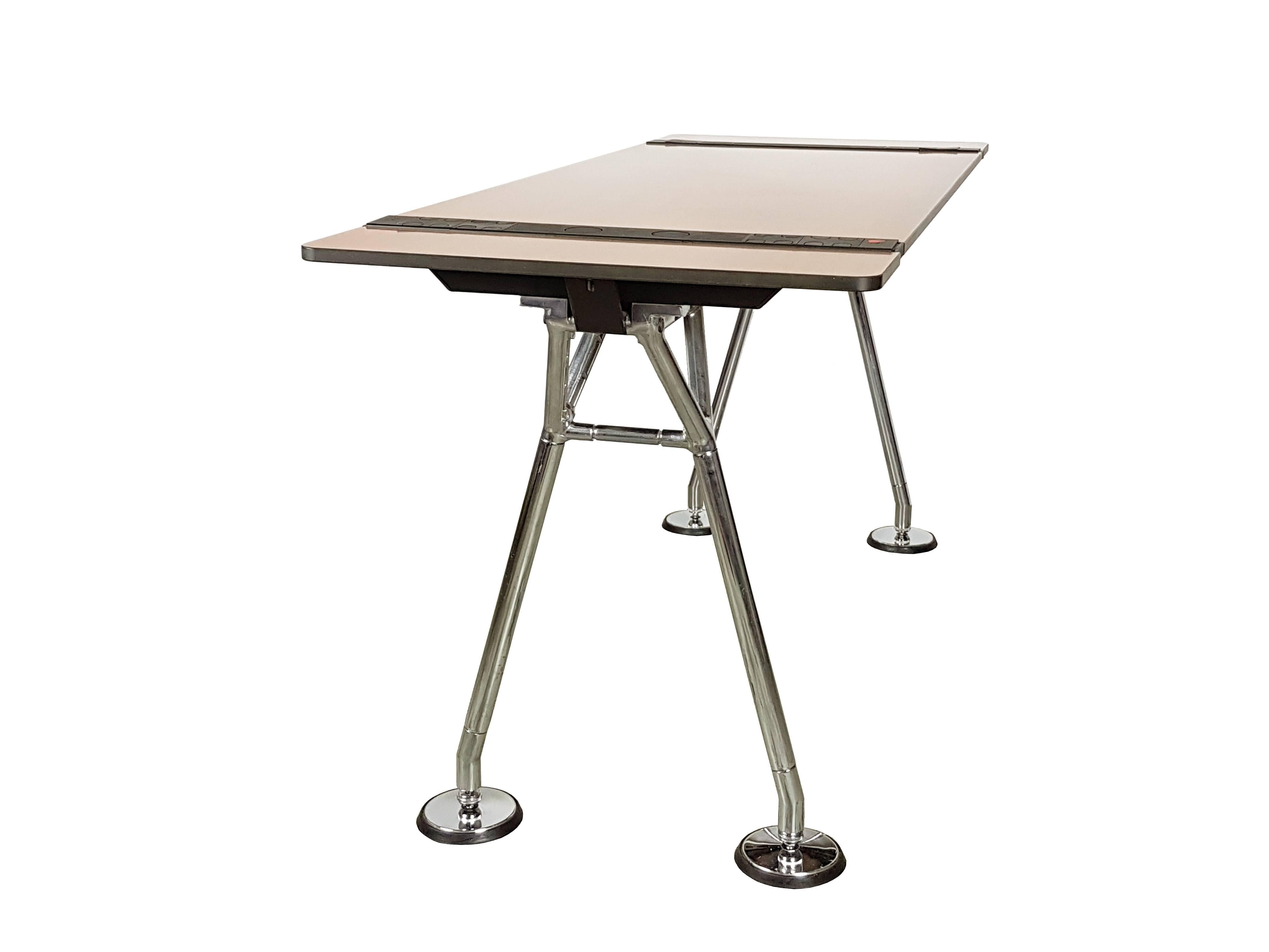 This desk was designed by Sir Norman Foster and produced in Italy by Tecno in 1987. The solid laminated top in a faux bois (fake wood) version, stands on a chromed metal frame with rubber adjustable feet. Its top features black caps to hide and tidy