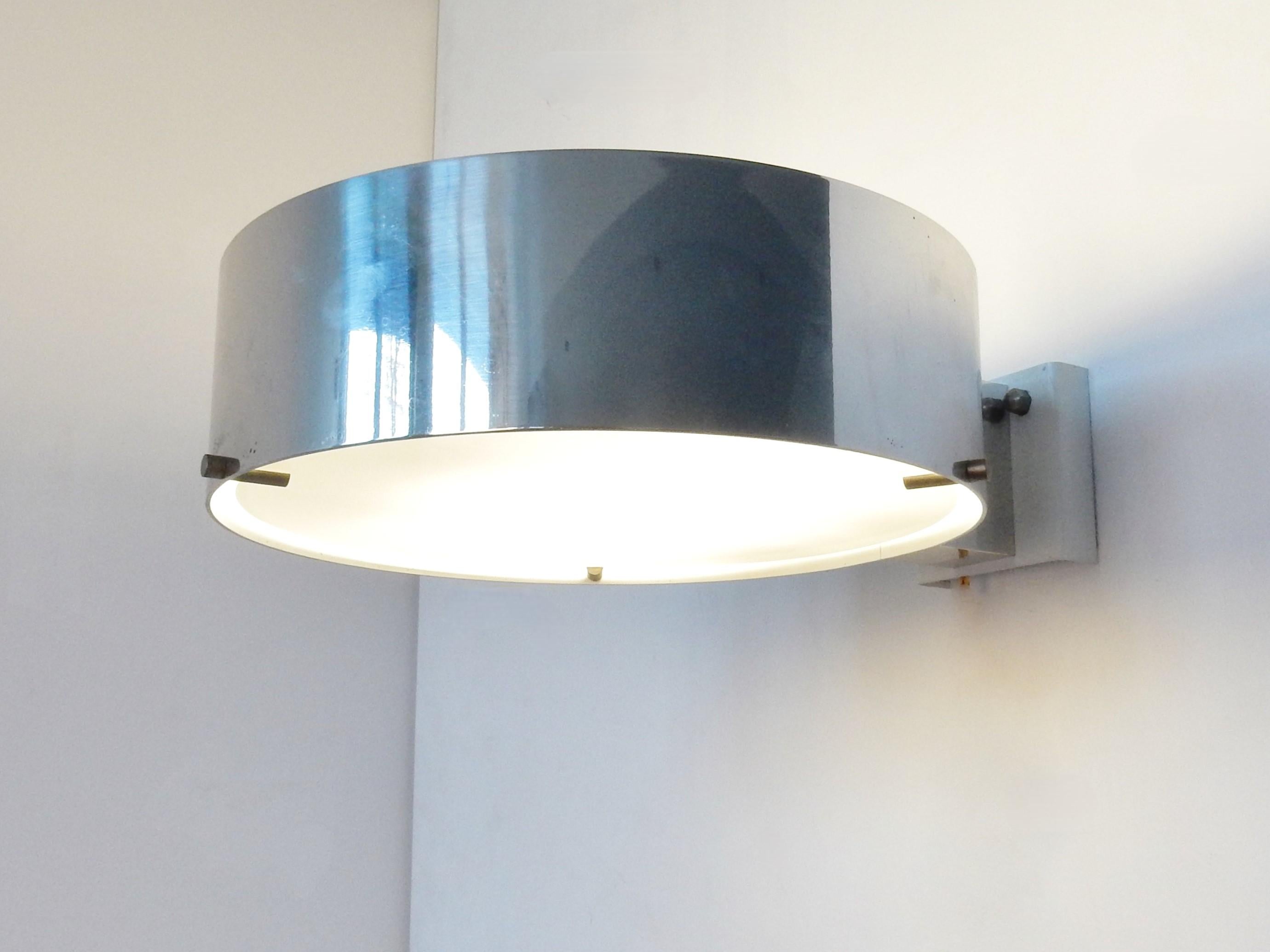Esta impresionante y rara lámpara de pared es un diseño de Bruno Gatta para Stilnovo de la década de 1960. Consiste en un anillo cromado que tiene un difusor de cristal blanco en medio sujeto por 3 pasadores metálicos. Las lámparas difunden una