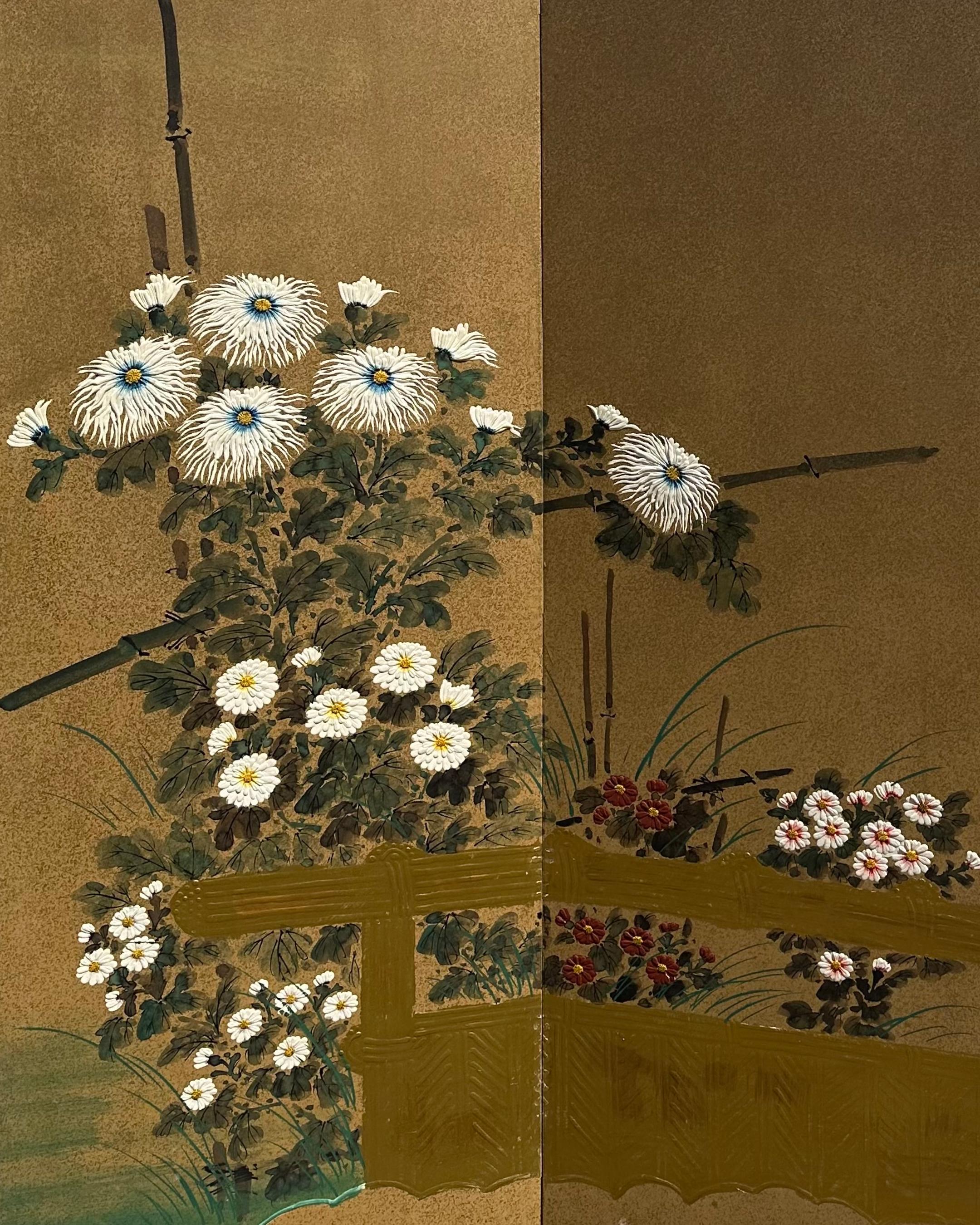 Vor einem schimmernden goldenen Hintergrund blühen Chrysanthemen in Weiß, Karminrot und Gelb - Blumen, die in der japanischen Kultur Langlebigkeit, Adel und den ewigen Kreislauf des Lebens symbolisieren. Gestützt von Bambuspfählen und umrahmt von