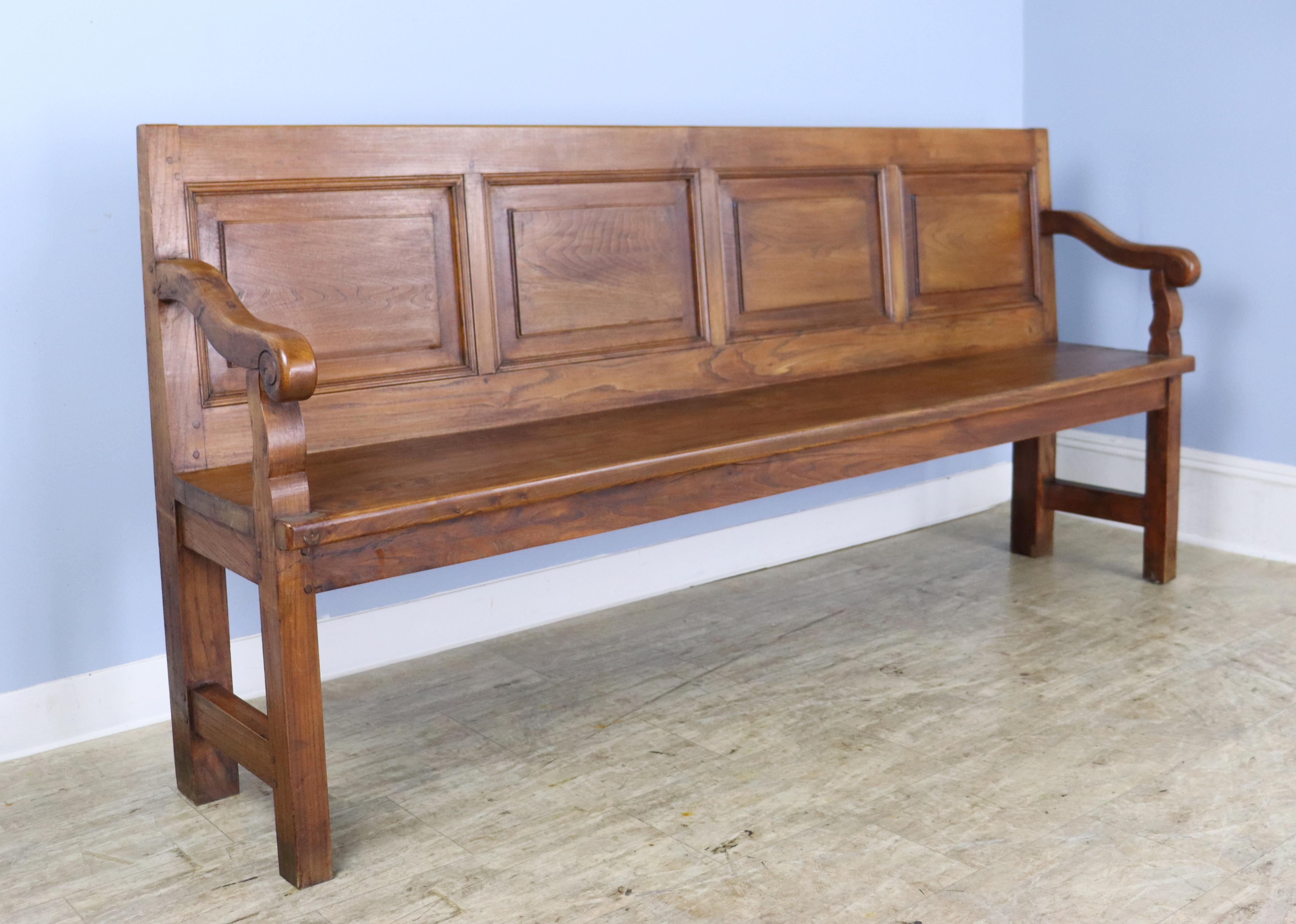 A handsome French elm bench with graceful curved arms and four inset panels across the back.  Marvelous elm grain and nice patina.  Slightly reclined back is quite comfortable.  Would work in the hallway, mudroom, or as occasional seating anywhere.