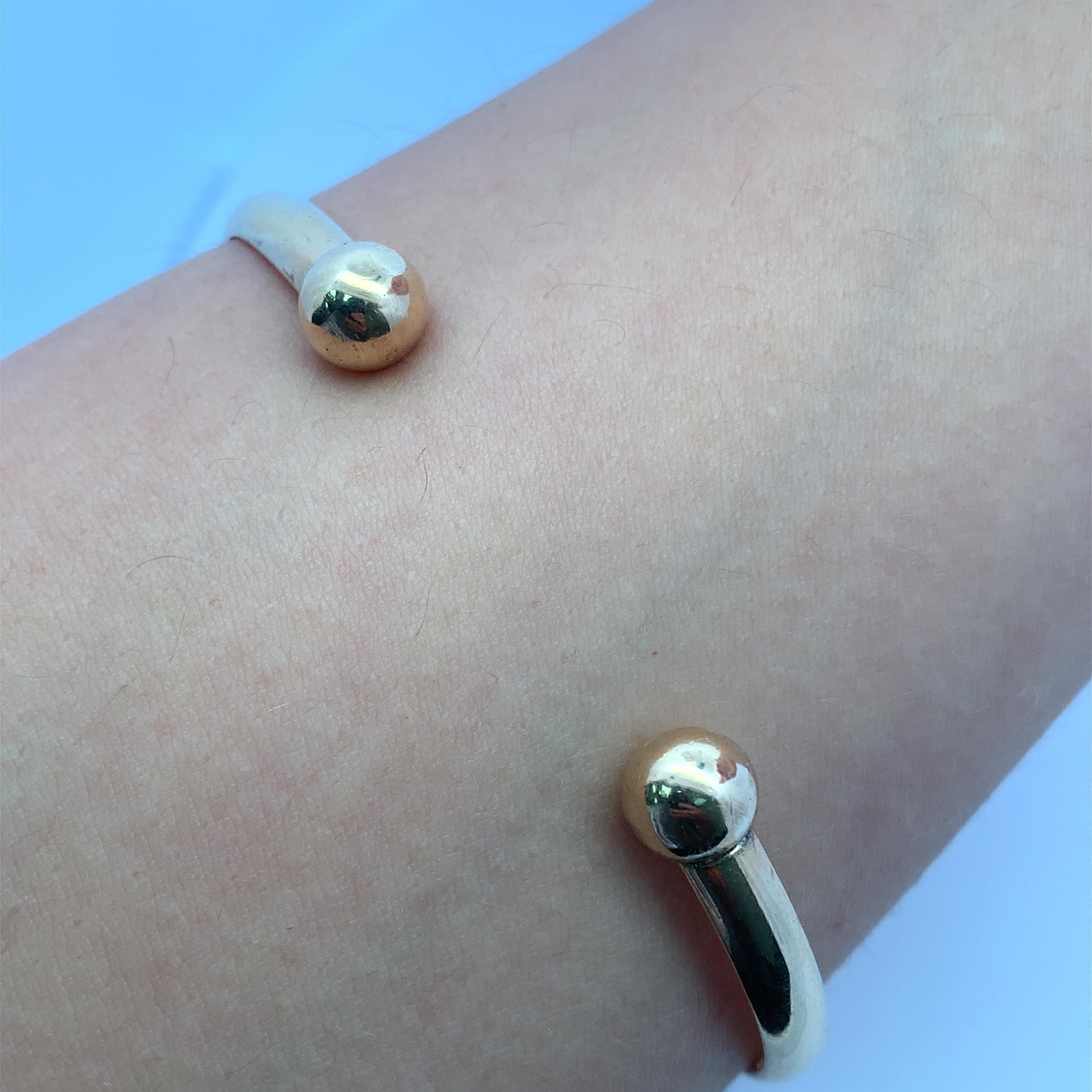 Découvrez l'élégance intemporelle de ce bracelet manchette en or, conçu pour rehausser n'importe quelle tenue. Son style minimaliste présente deux sphères polies qui ajoutent une touche de sophistication, ce qui la rend parfaite pour les occasions