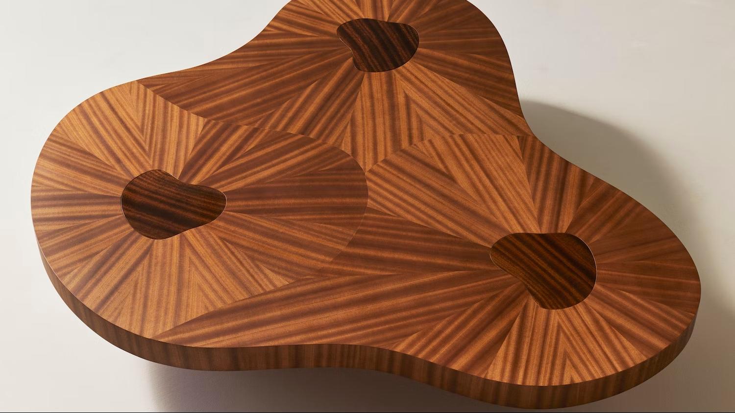 An evolution of the Cloud Table, showcasing the same gravity-softening design but with stouter proportions. The high-gloss table legs are uniquely shaped, creating the appearance of placid pools on the tabletop. The stunning marquetry work changes